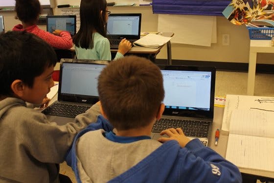 2 boys using laptops in a classroom