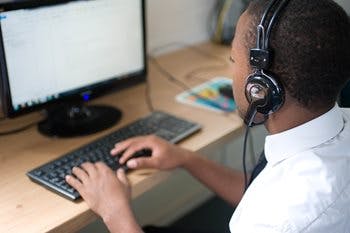 Boy in school uniform wearing headphones working on a computer