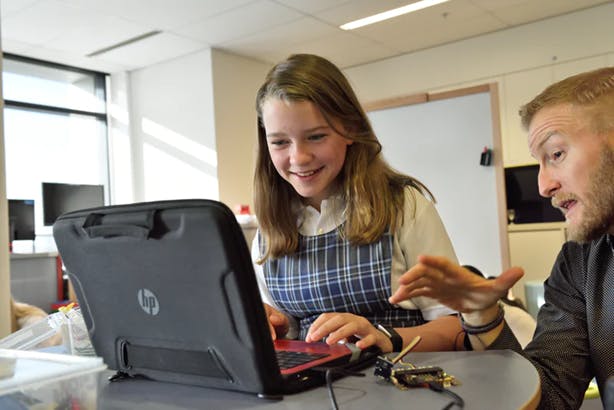 Student using computer in classroom with teacher