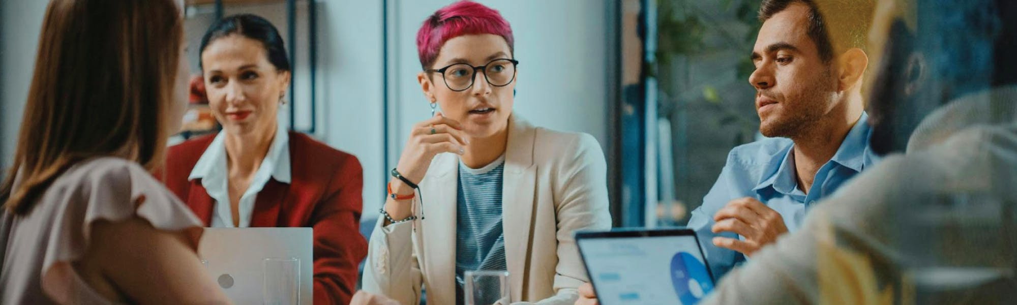 Image of 5 employees dressed smartly and talking around a desk