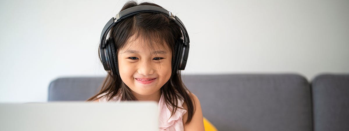 young child reading from a laptop with headphones on