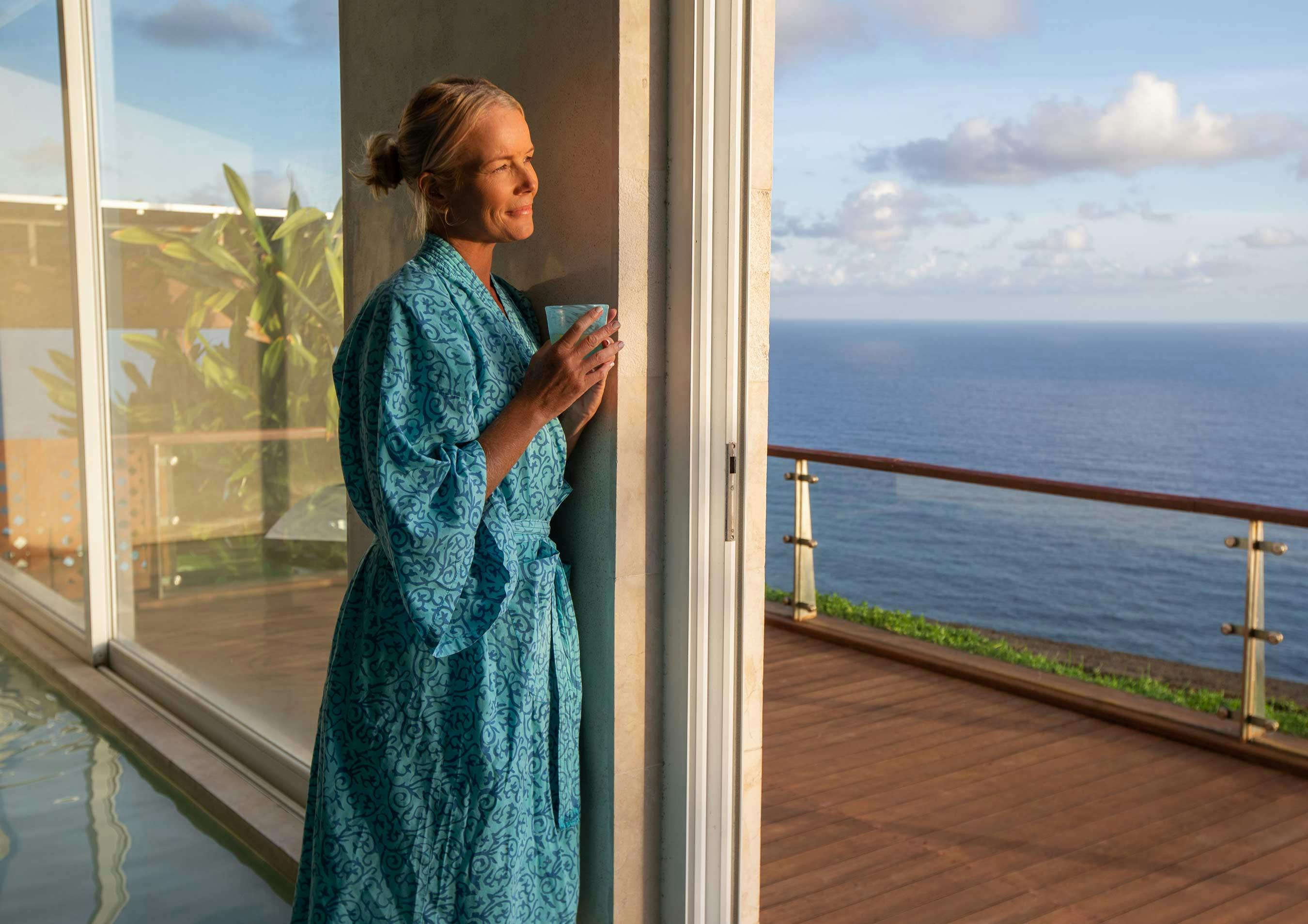 woman standing holding a cup of tea, looking out at the view in luxurious spa in Bali