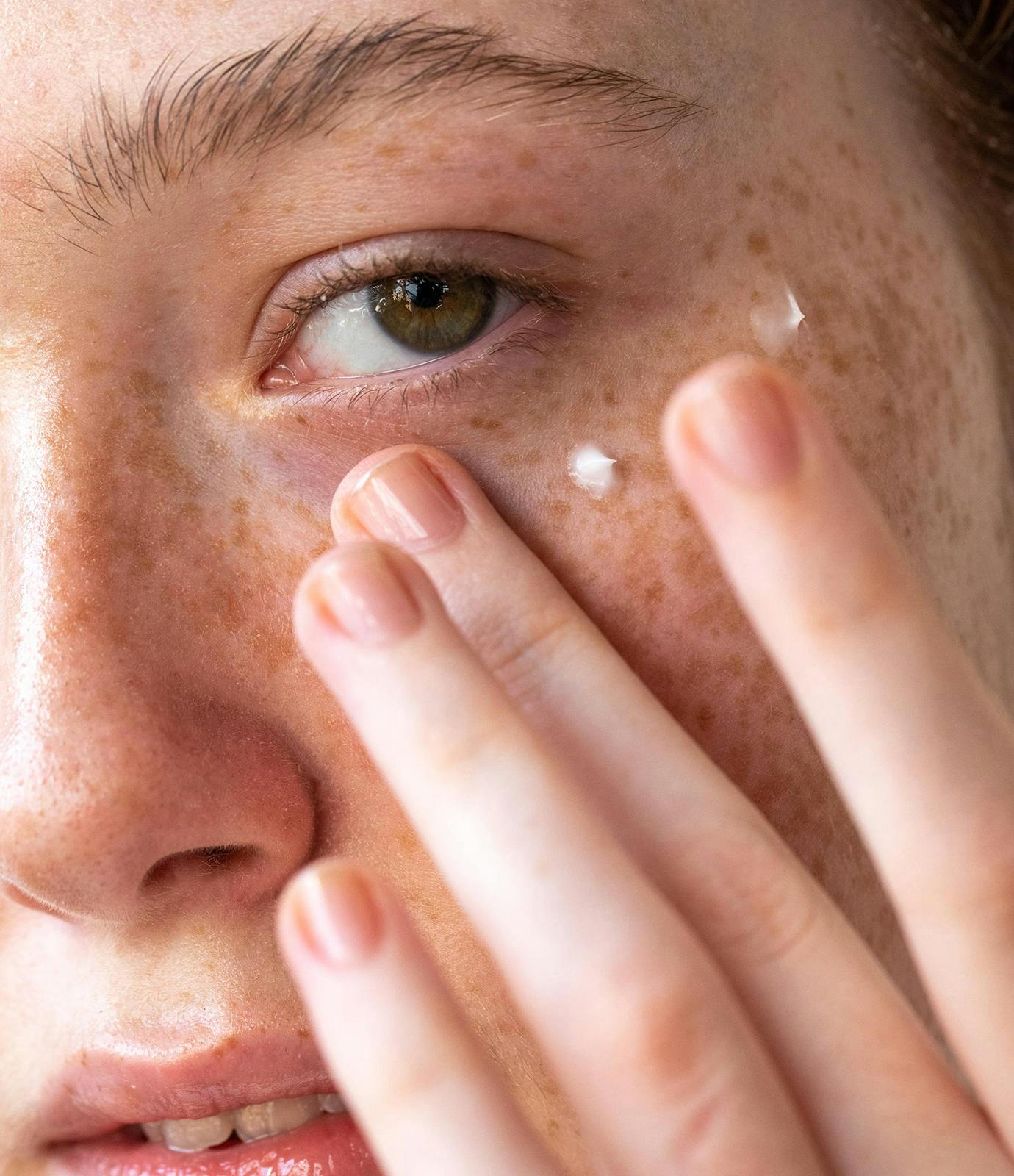 Photo of model applying The Outset's Smoothing Vitamin C Eye + Expression Lines Cream underneath her eye