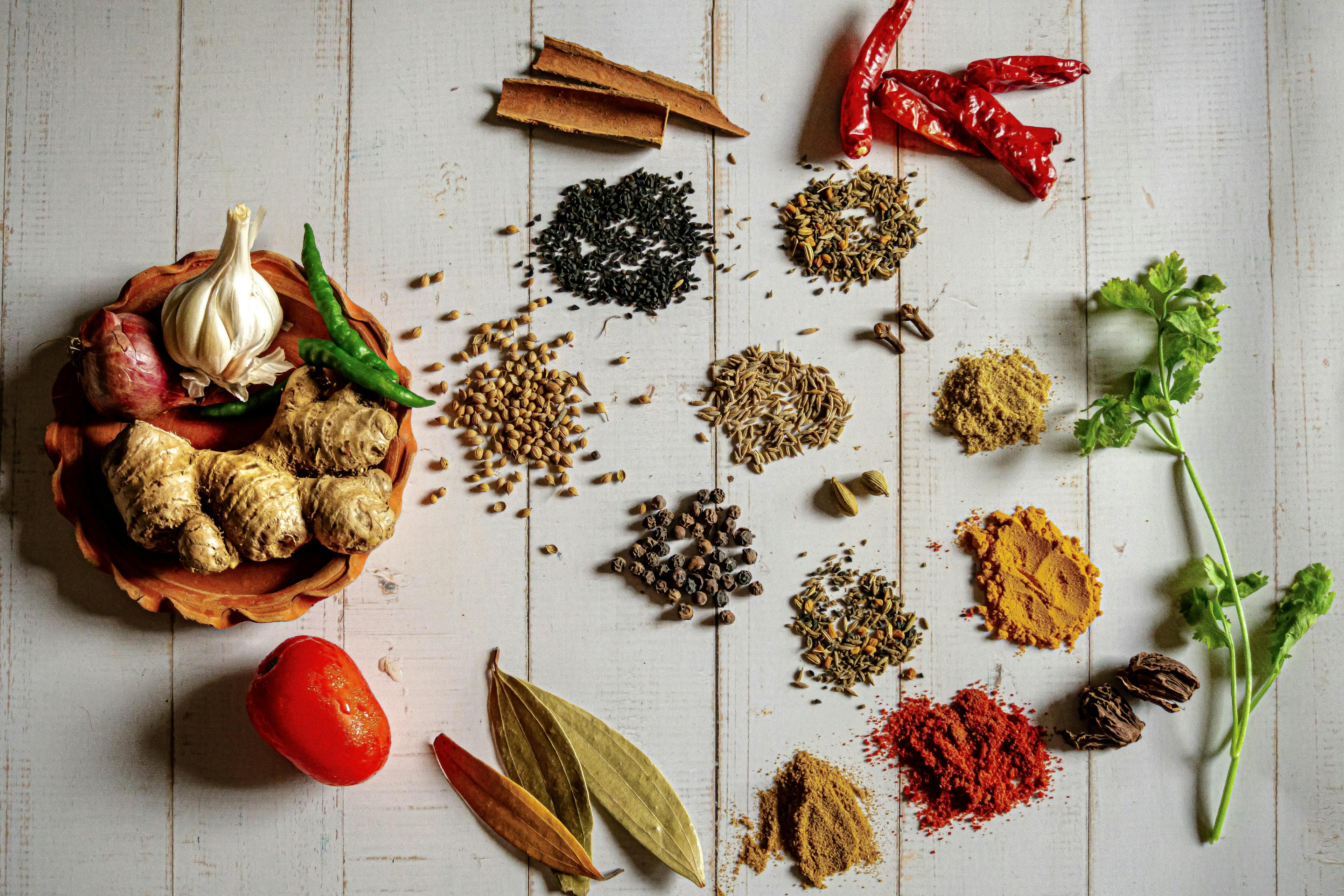 different ground seasonings on table with a bowl of whole spices.