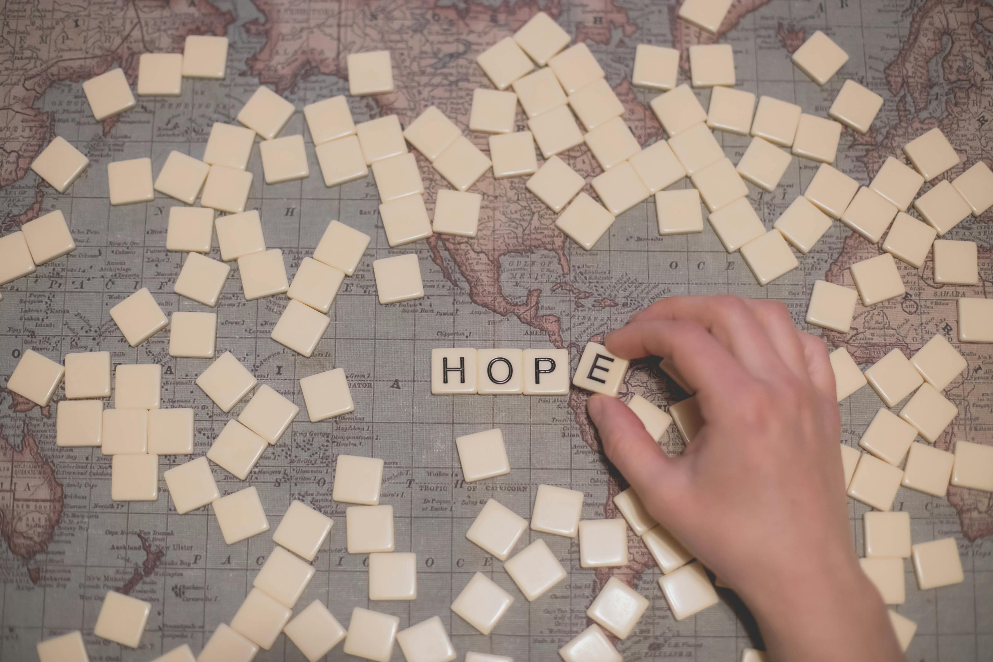 person's hand holding square blocks arranging the word hope  on top of a map with other blocks surrounding word.