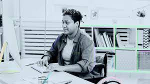person in a wheelchair sitting at desk in front of computer typing in office.