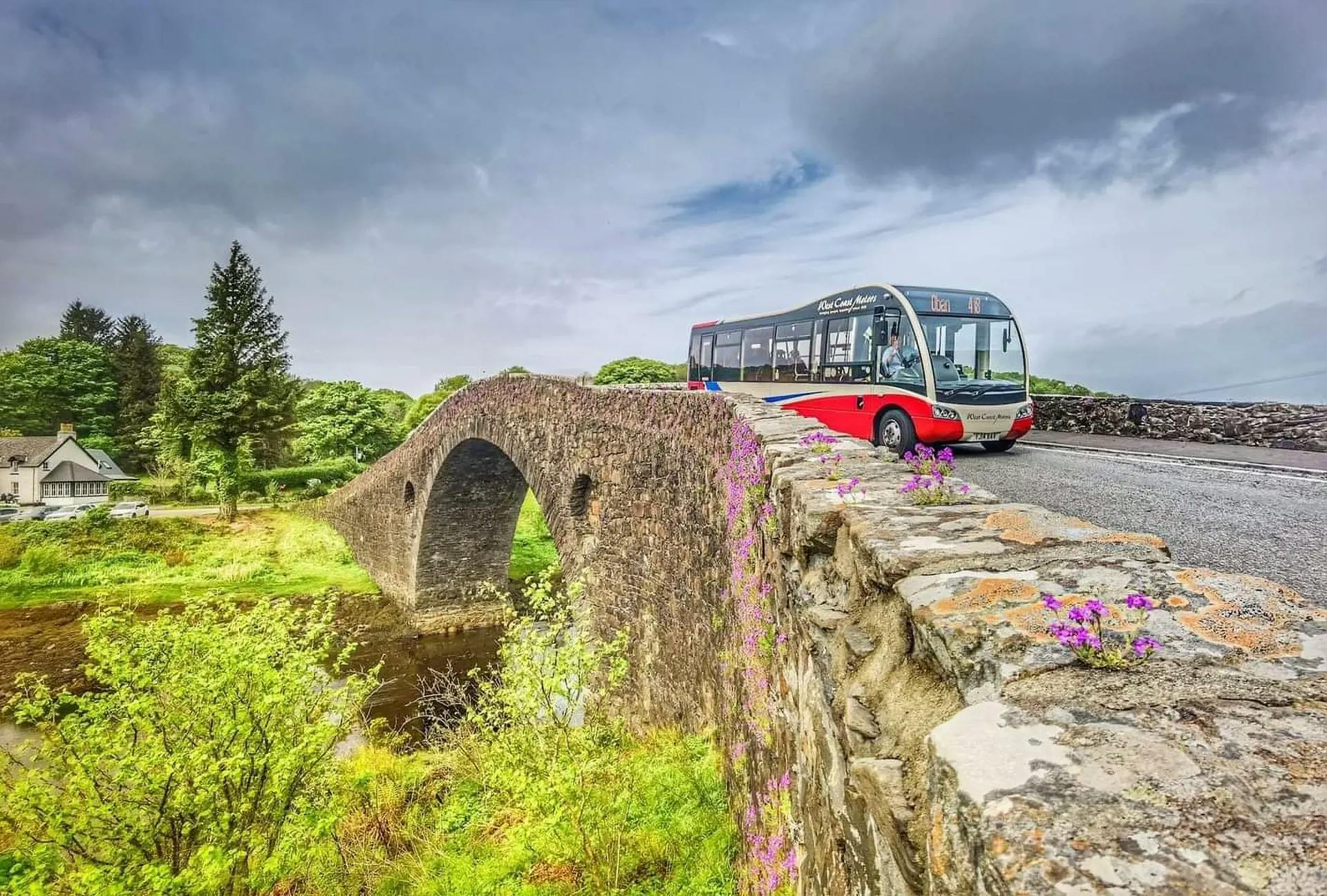 A West Coast Motors vehicle drives over a bridge in rural Scotland.