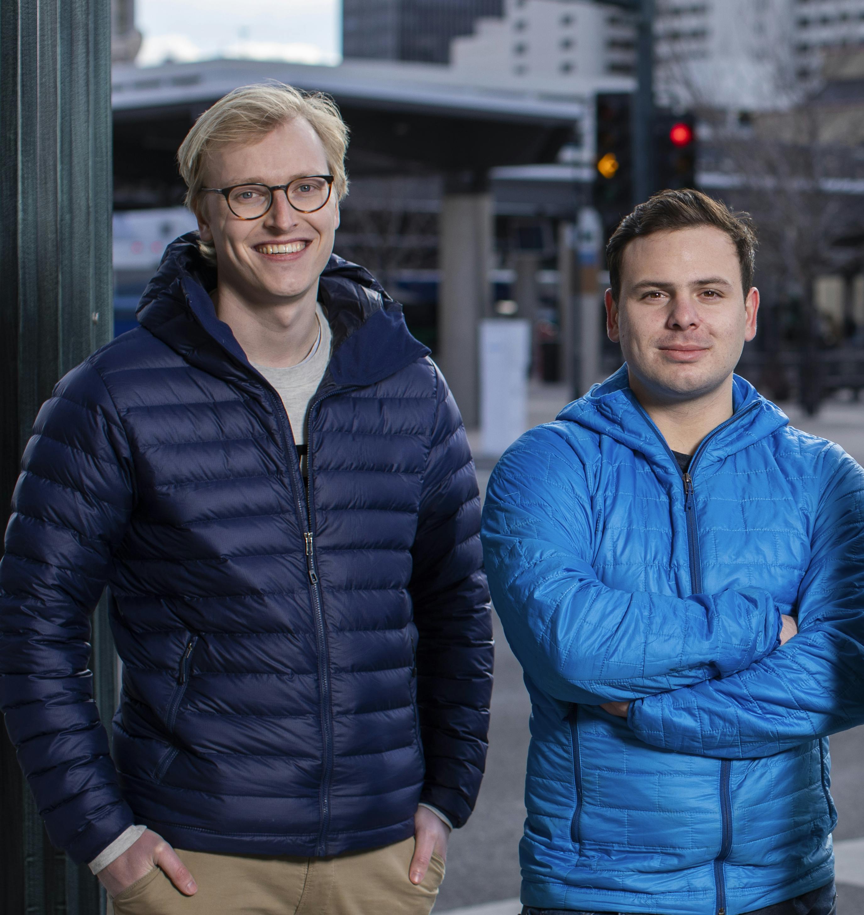 Menno van der Zee and Alex Wallar stand next to each other in front of a city street.