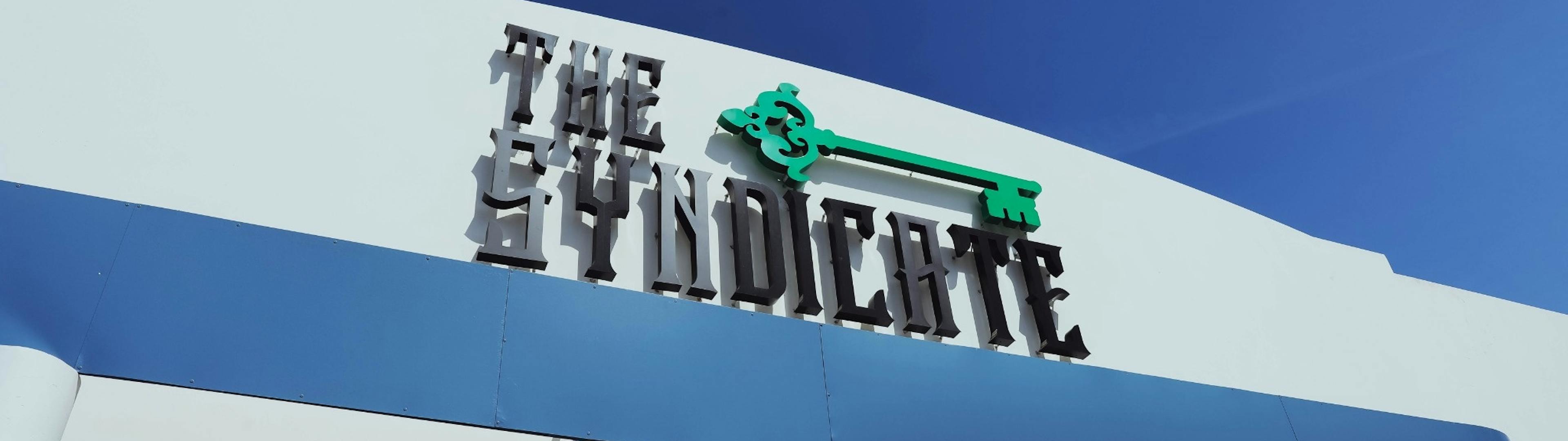 Exterior facade of The Syndicate Lake Elsinore #2 featuring bold signage and a clean blue awning.
