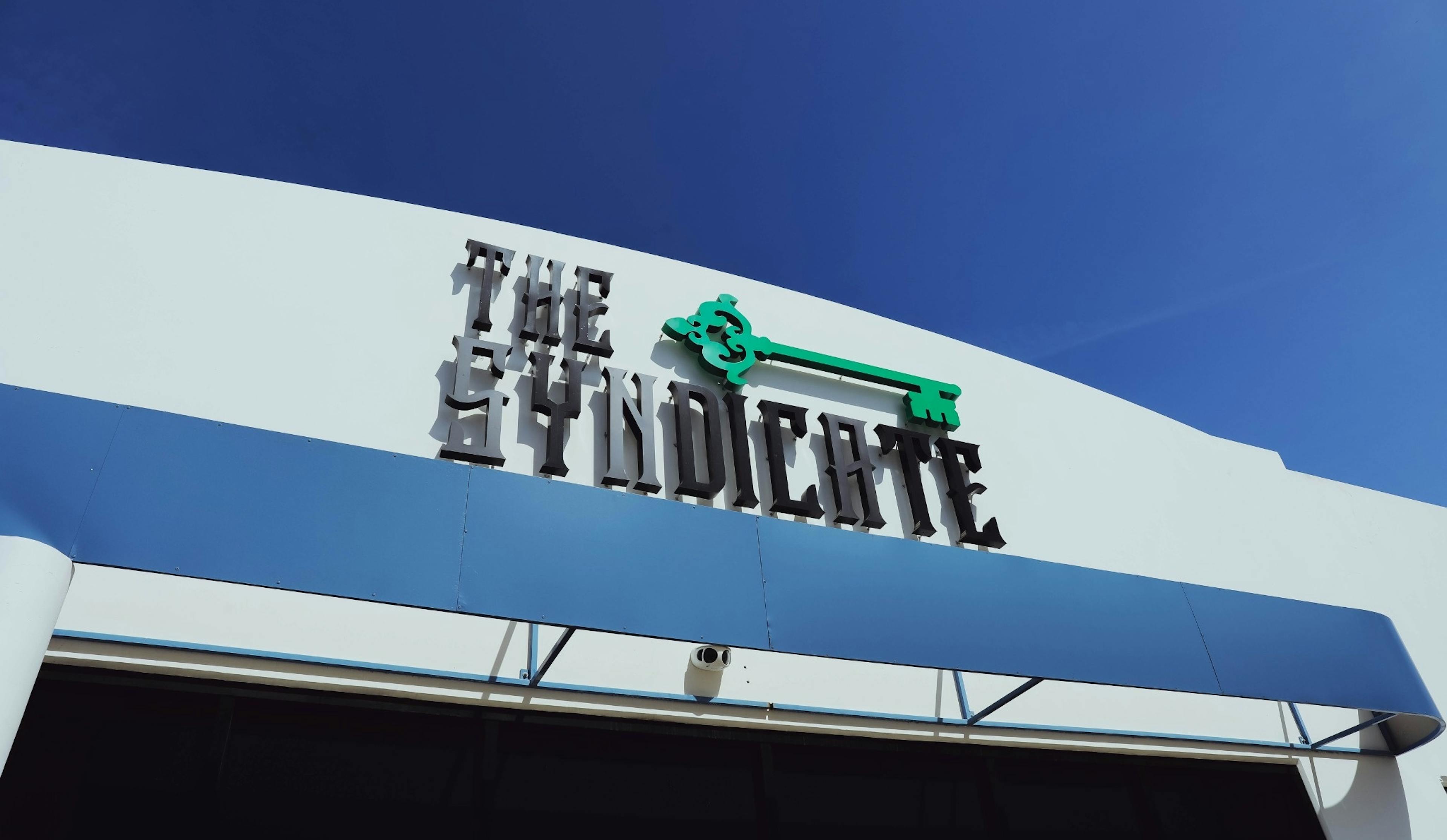 Exterior facade of The Syndicate Lake Elsinore #2 featuring bold signage and a clean blue awning.