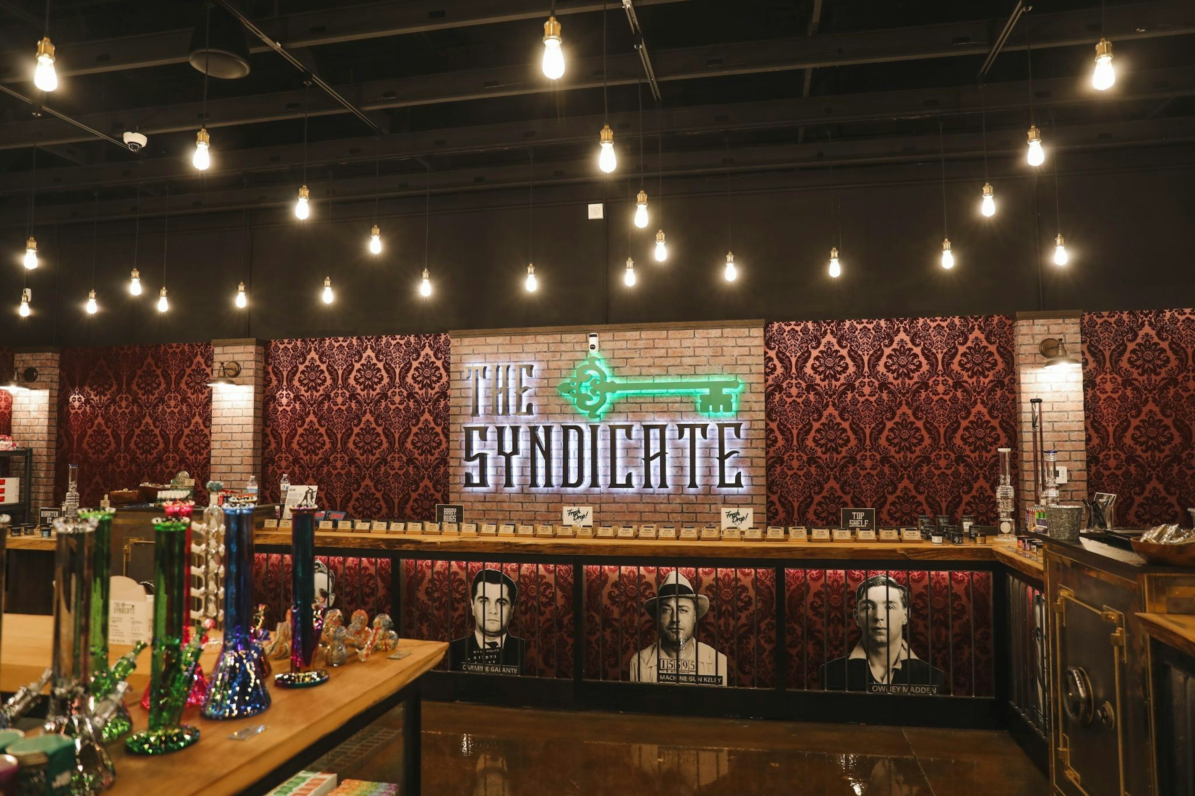 Central front counter at The Syndicate Lake Elsinore #2 with illuminated logo sign and classic decor.