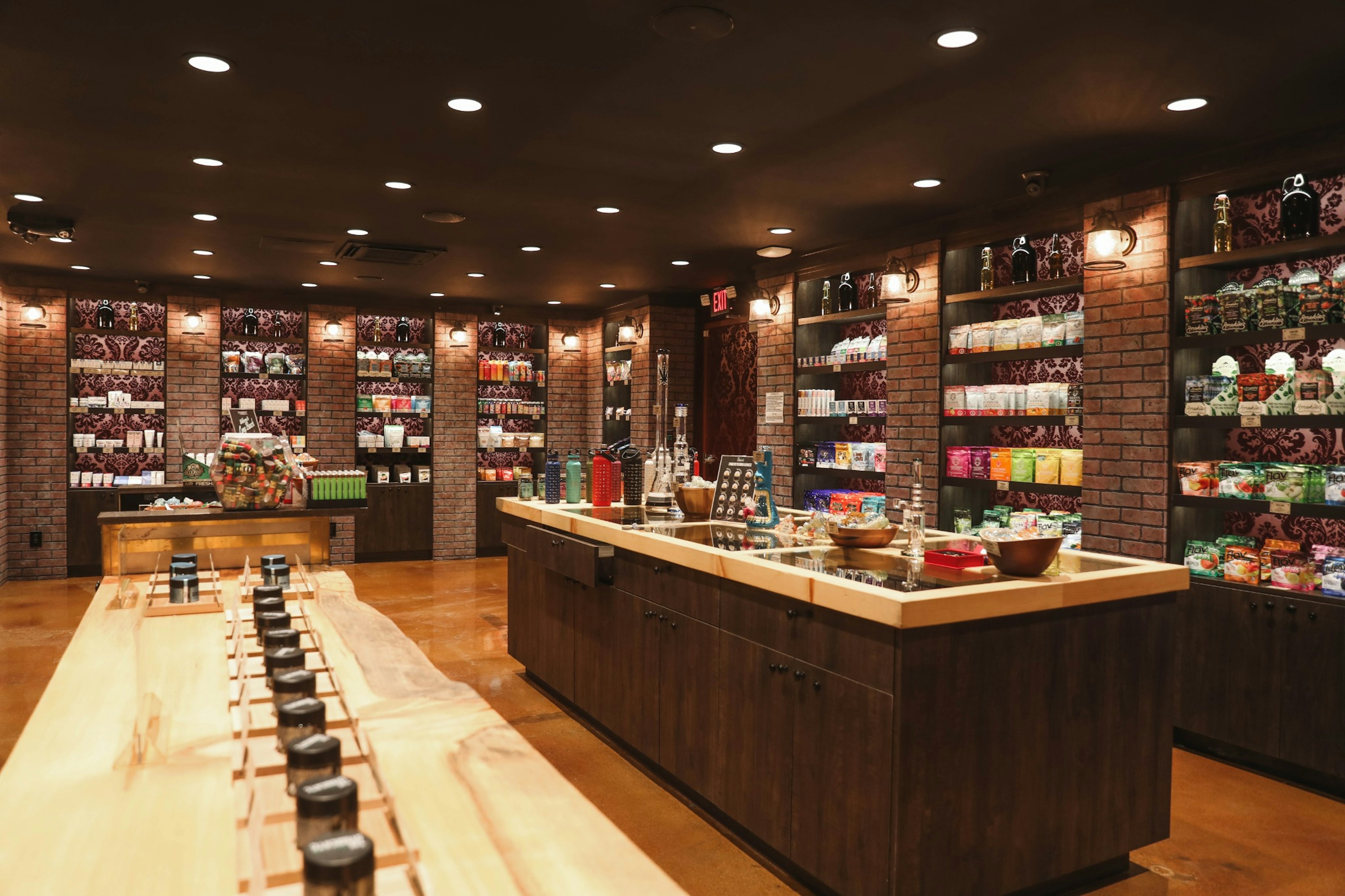 Deep perspective of the store interior showing long wooden table with sampling jars, surrounding shelves filled with products, and soft overhead lighting.
