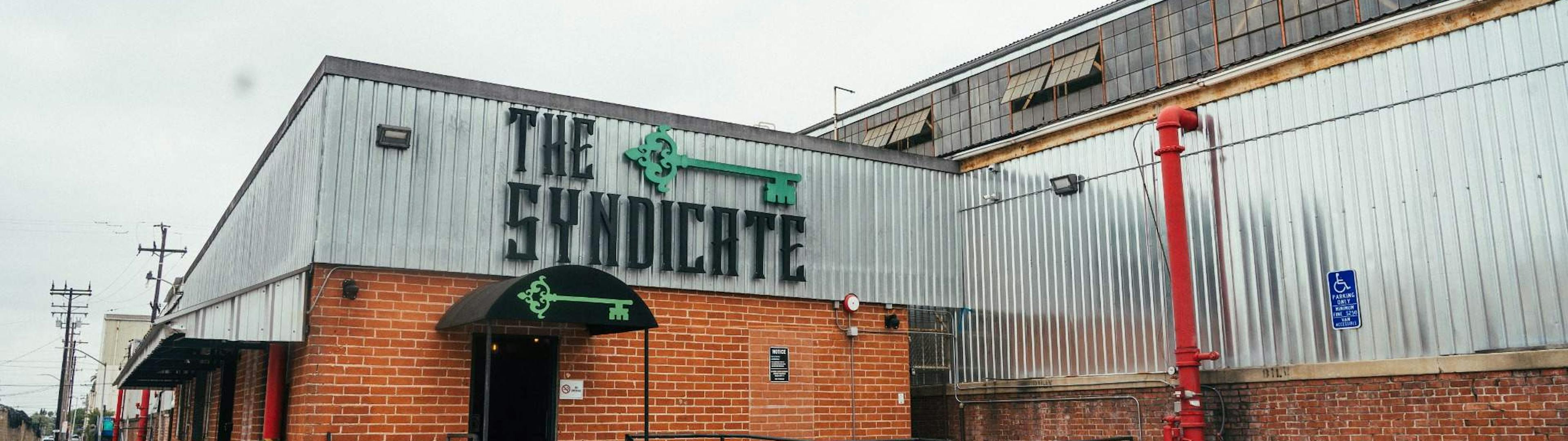 Wide exterior shot of The Syndicate Huntington Park location showcasing the building and branded signage.