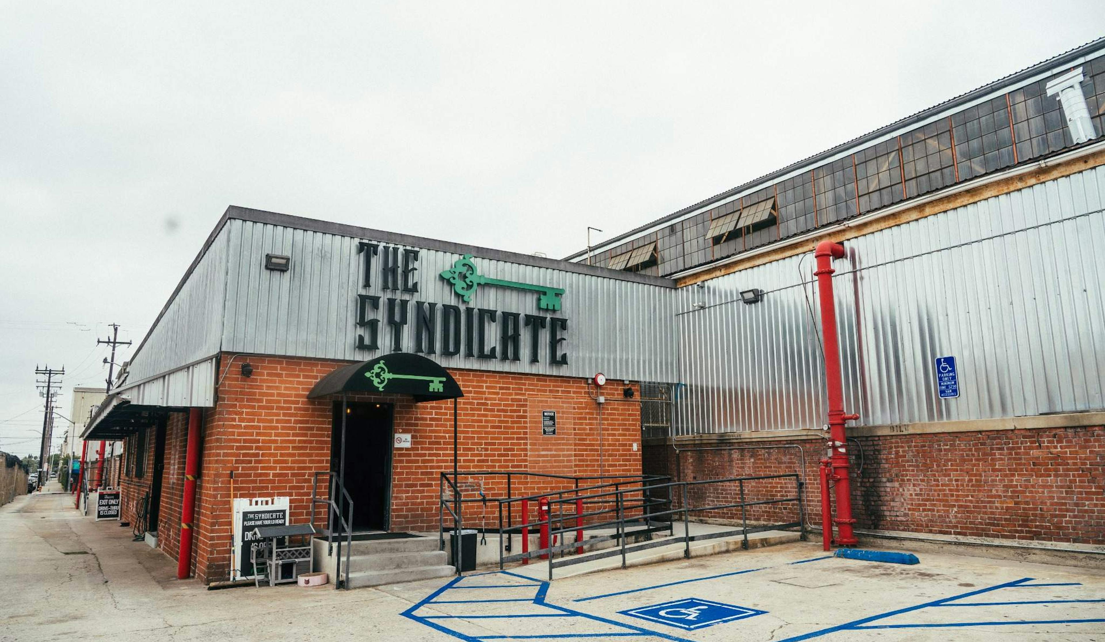 Wide exterior shot of The Syndicate Huntington Park location showcasing the building and branded signage.