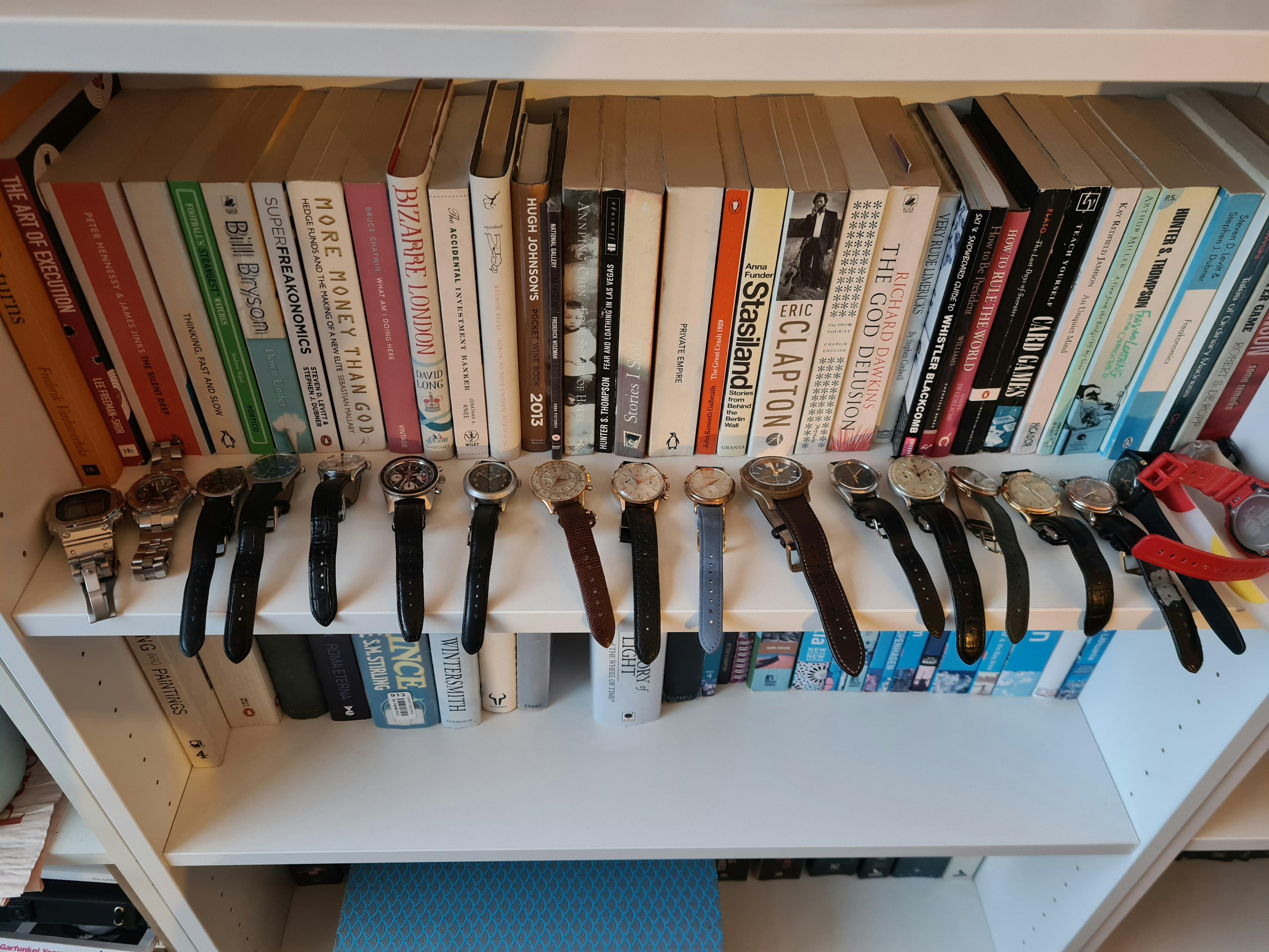 A watch collection lined up on a bookshelf with books behind it