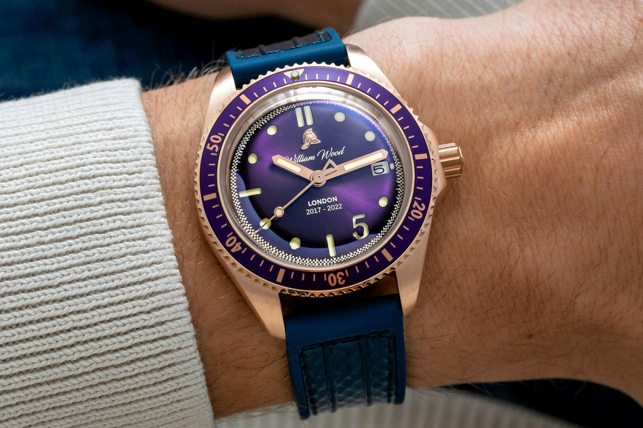 A Purple and bronze watch from william wood with striking colurs and an unusualy single number five on the dial, with a dark blue rubber strap.