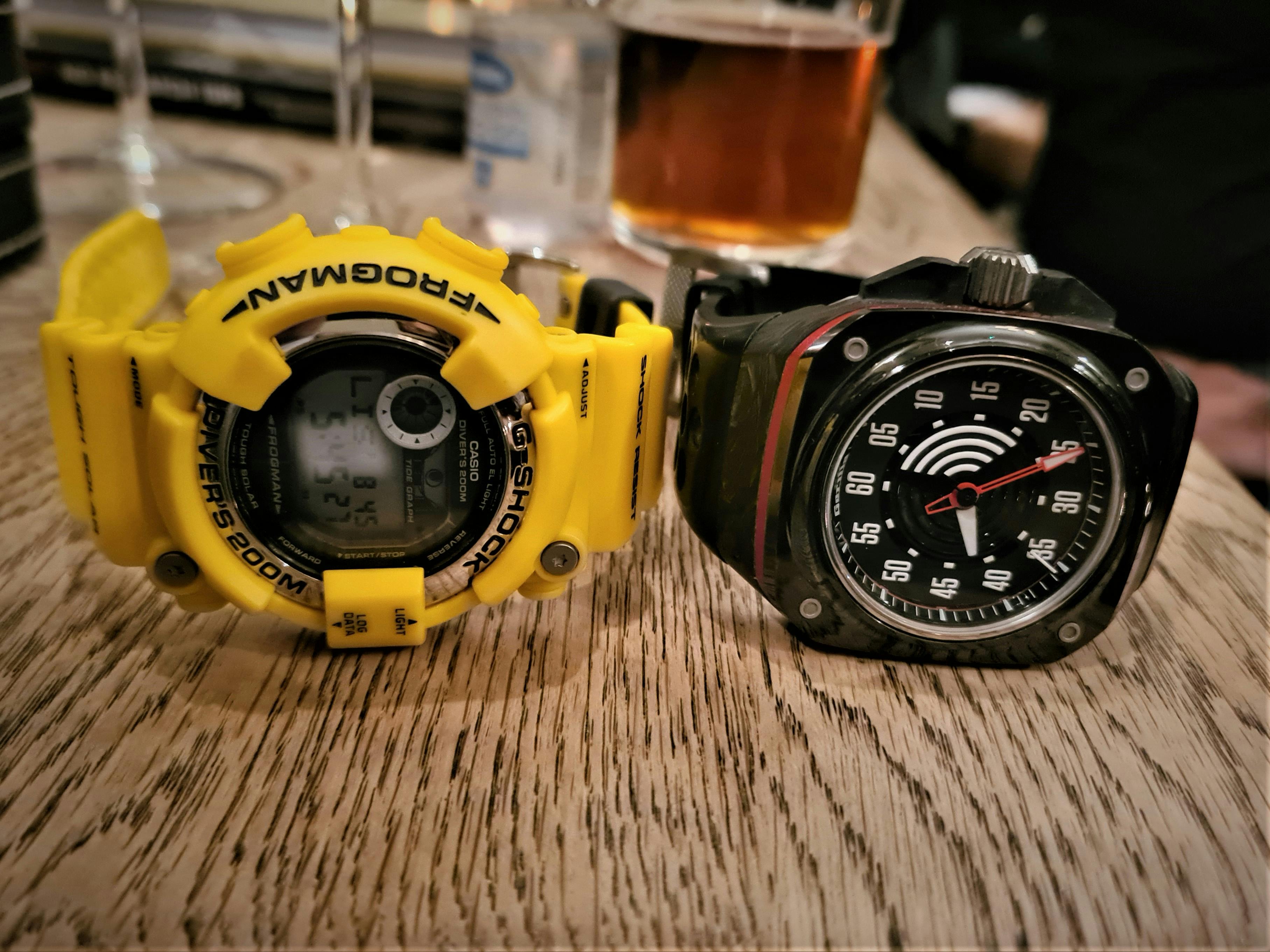 Two watches side by side on a table at a watch meetup event, one yellow G-Shock, one Black Gorilla Fastback.
