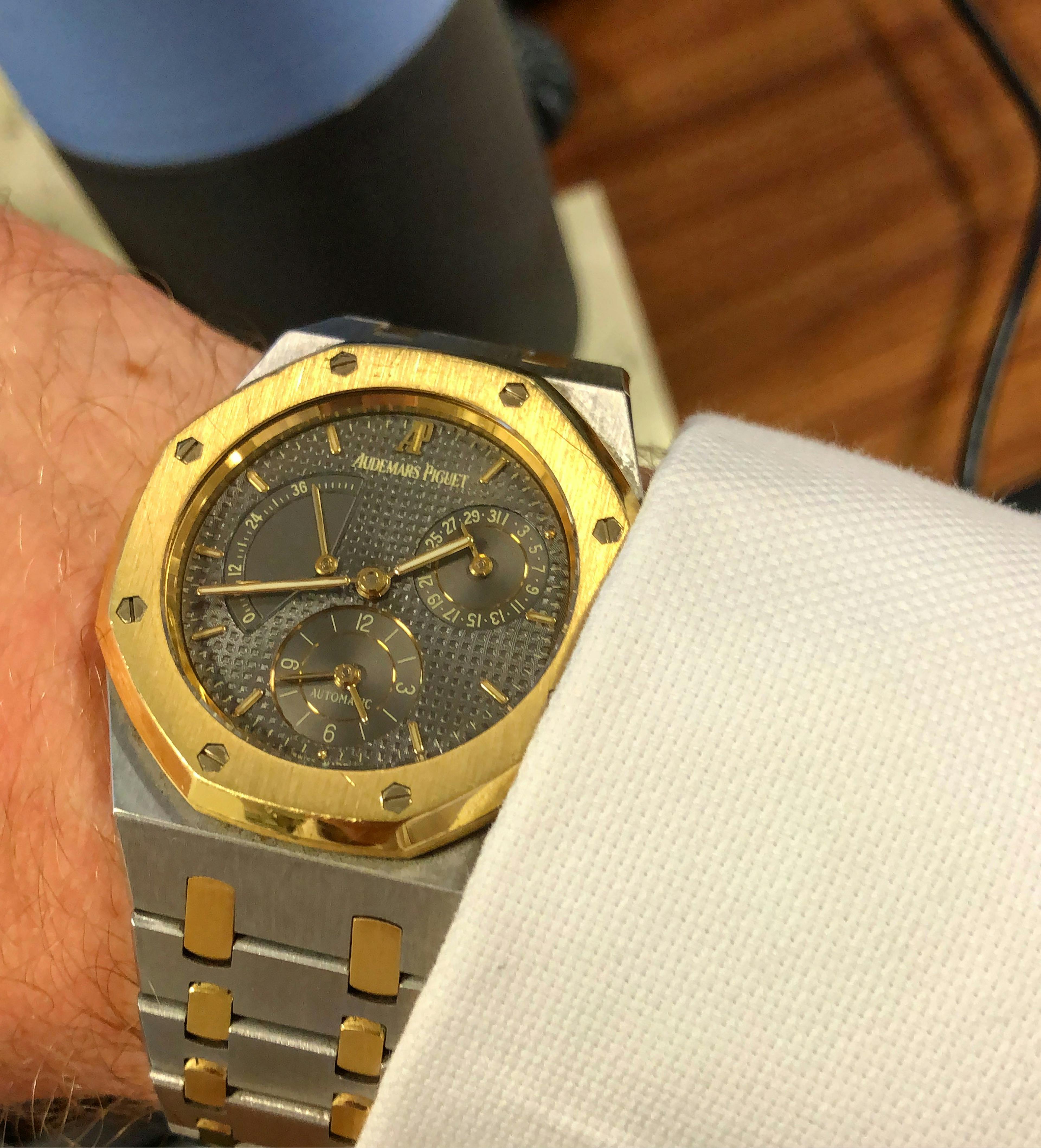 A bimetal steel and gold AP Rpyal Oak watch on a wrist with a grey dial and gold hands and indices, three subdials and a white shirt cuff visible