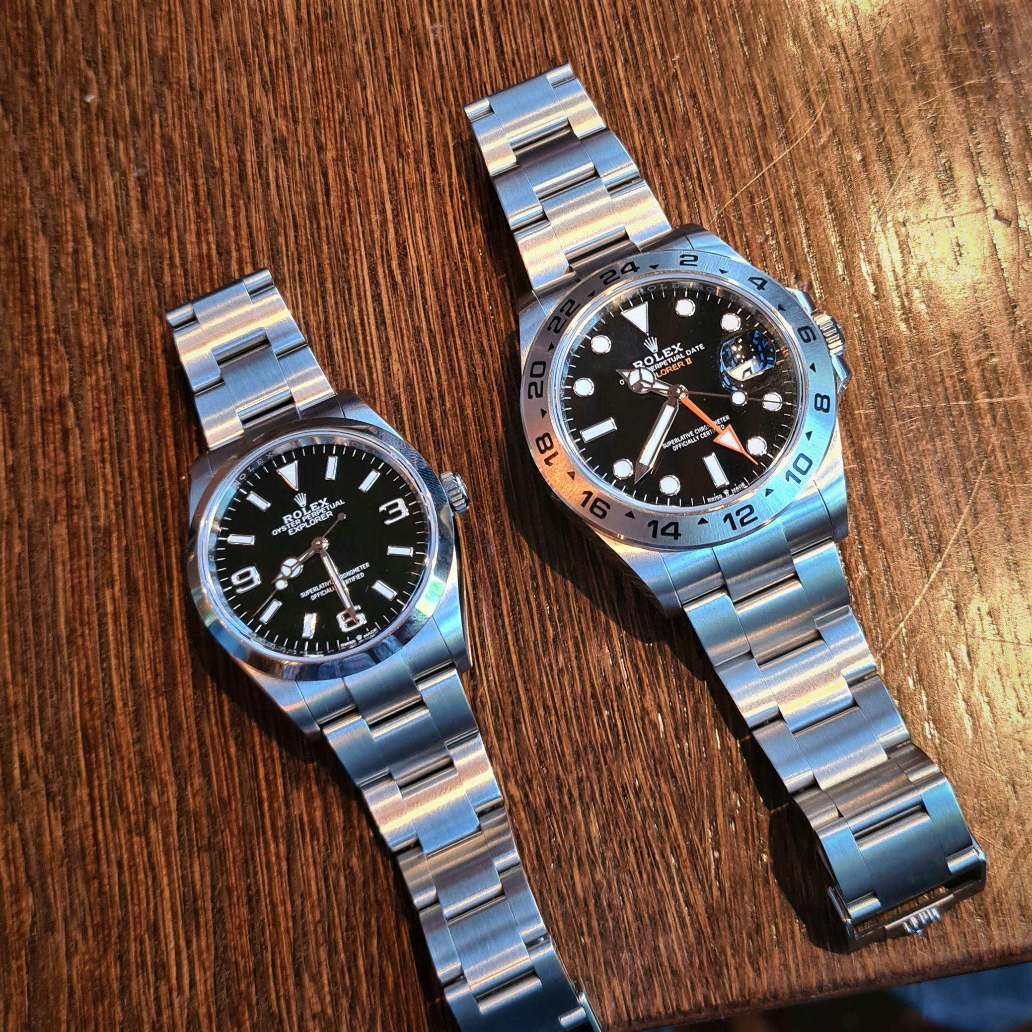 Two Rolex steel watches lying on a table with black faces and polished bezels