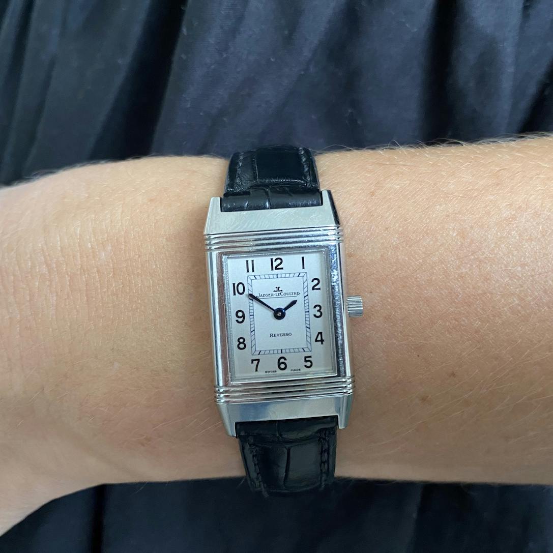 Rectangular JLC Reverso watch in steel with two tone dial of cream and white with black hands on a black leather strap.