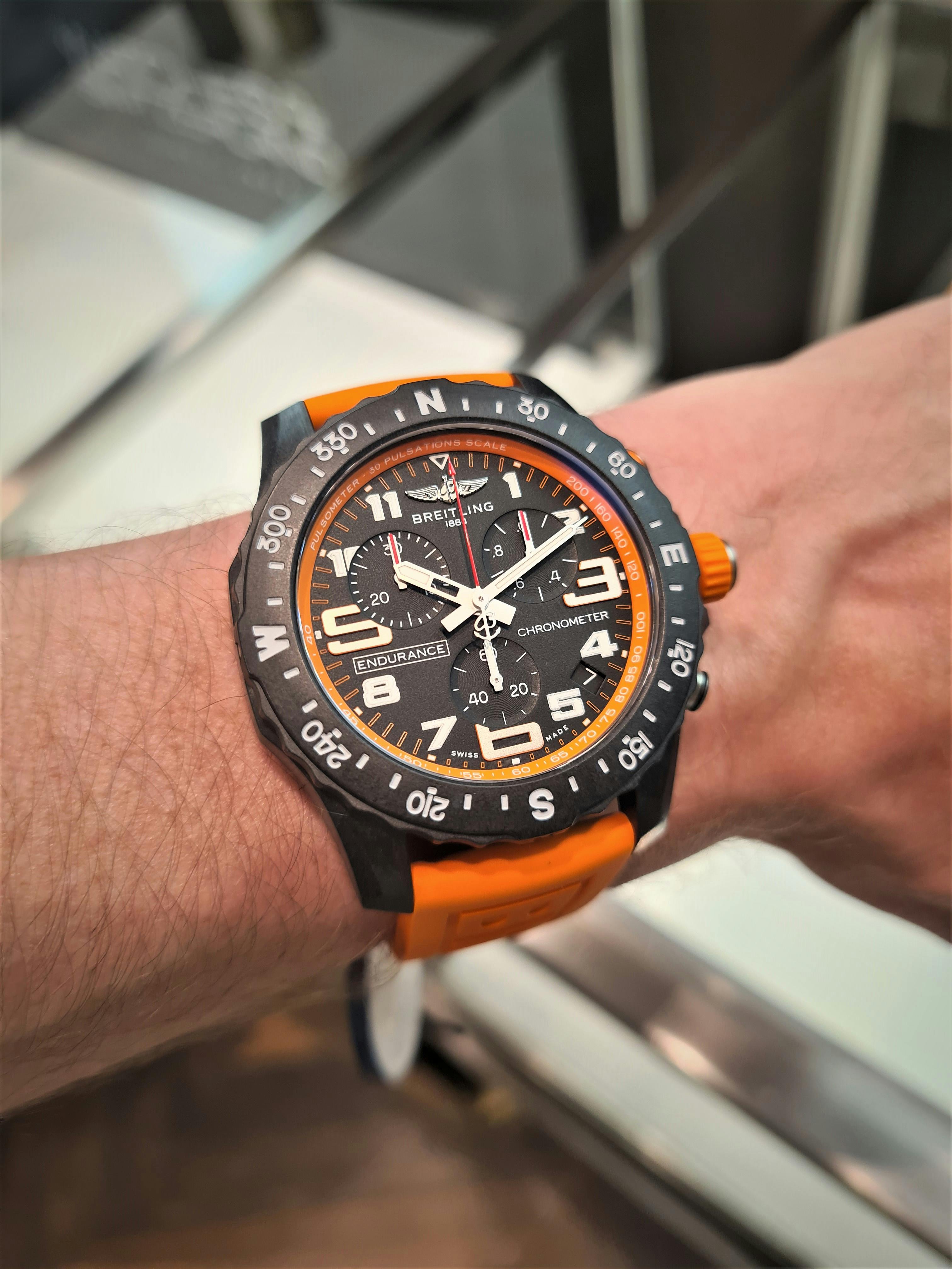 Grey and orange Breitling watch with large white numbers and white hands