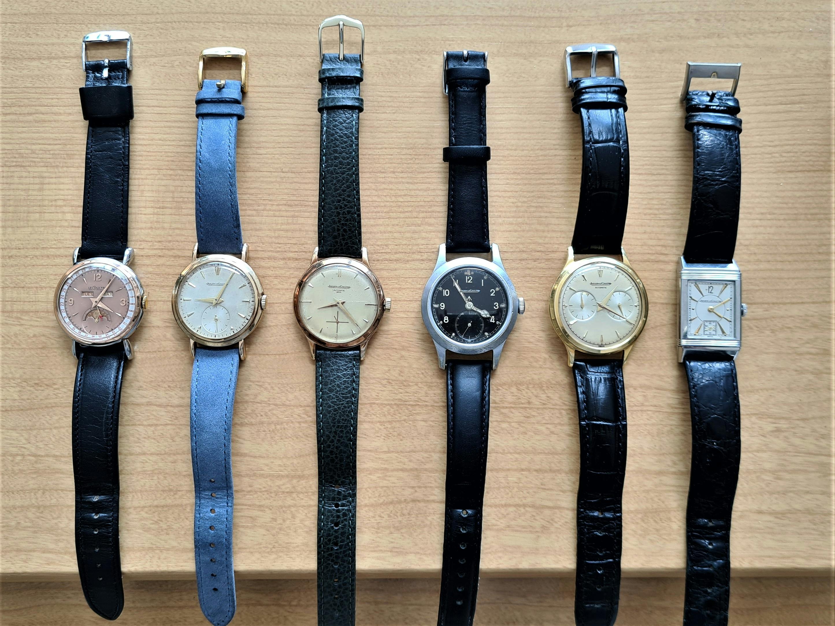 Group of six watches displayed on a table with different metal cases, dial colours and strap colours.