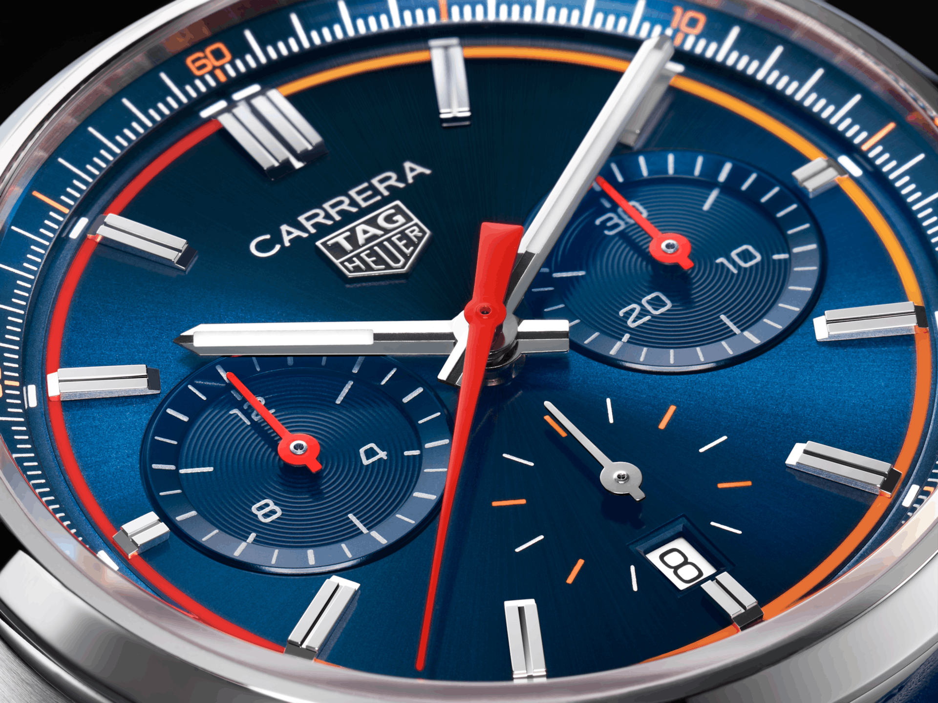 Dark blue dialled Tag hehuer carrera chronograph close up with bright red chronograph seconds hand, straight lumed steel hour and minude hands, and red and organe accents on the dial  inutes trach and the seconds subdial, with a small date window at the 6 o'clock position.