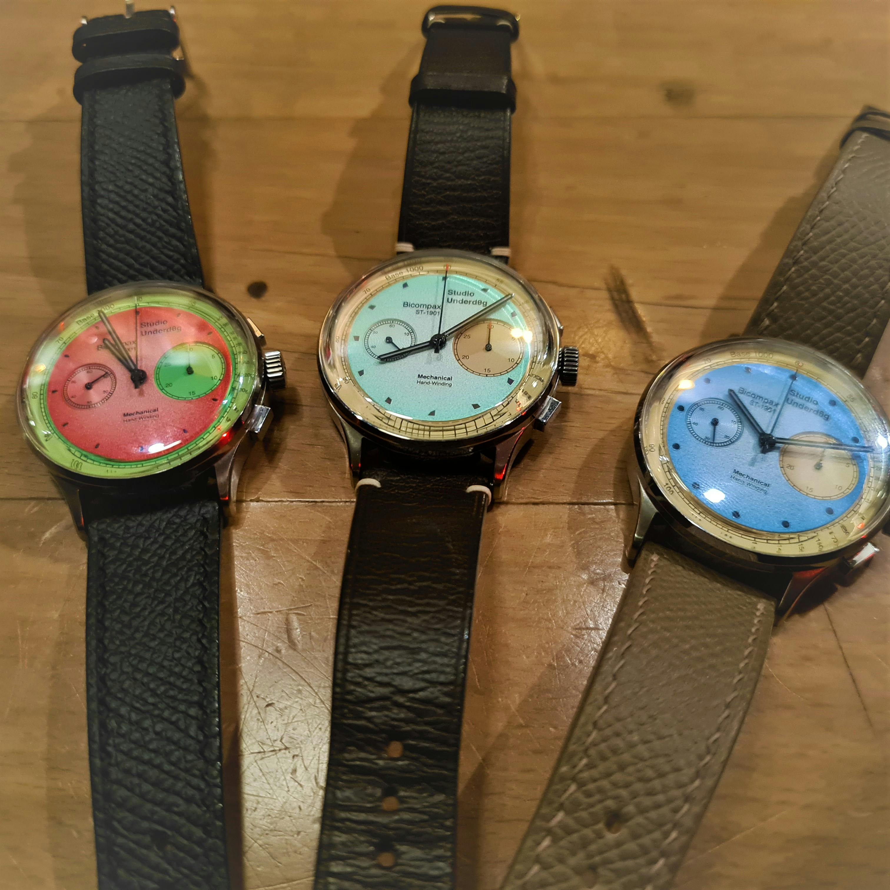 Three colourful watches lying on a table with brown straps, one in pink and green, one in light blue an yellow and one in sky blue and yellow, all from Studio Underdog