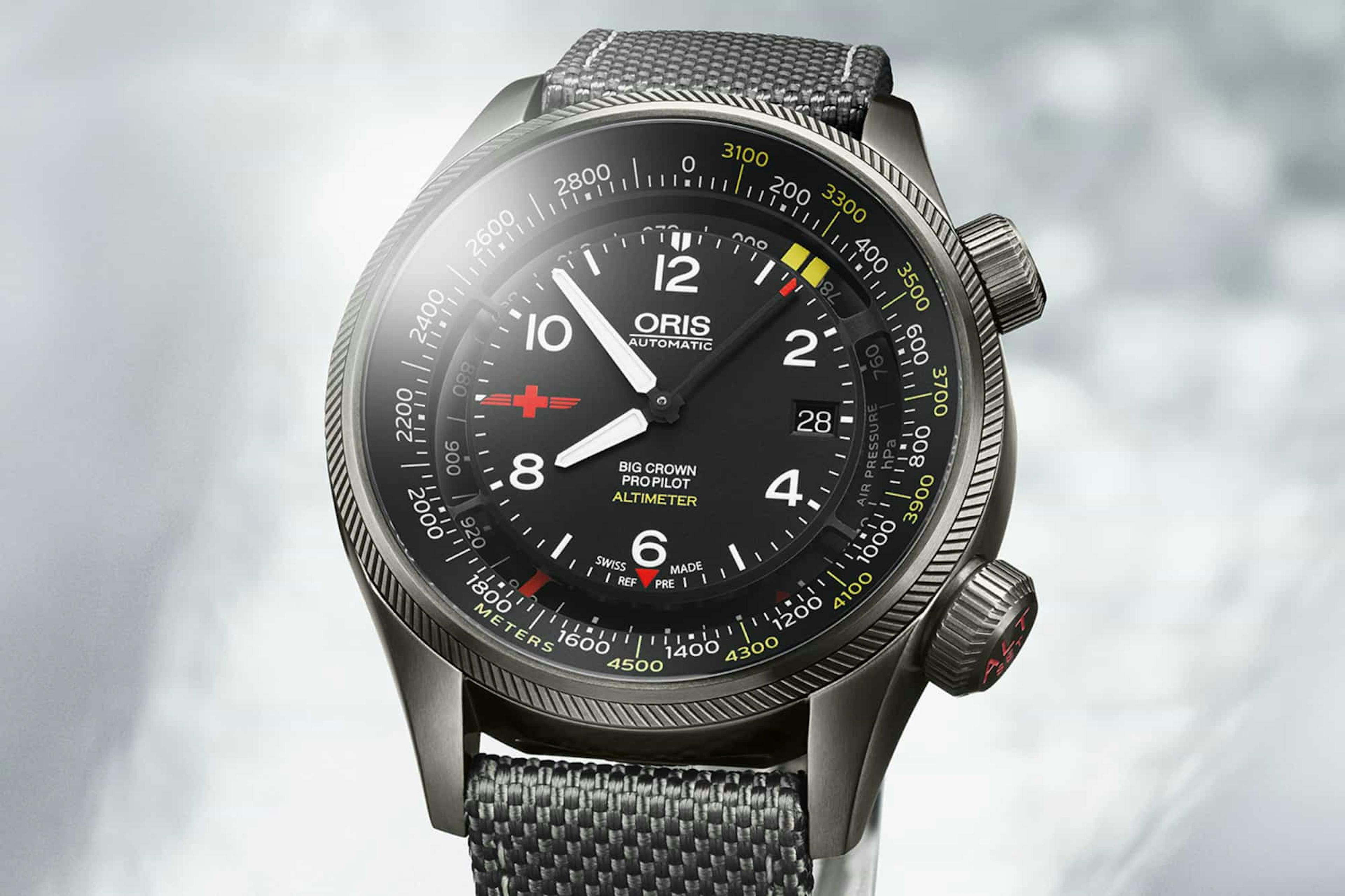 A large grey Oris ProPilot watch with black dial white numbers and hands, altimeter around the dial perimeter and accompanying scales in black and yellow, with two crowns on the right hand side of the case and a grey strap. 