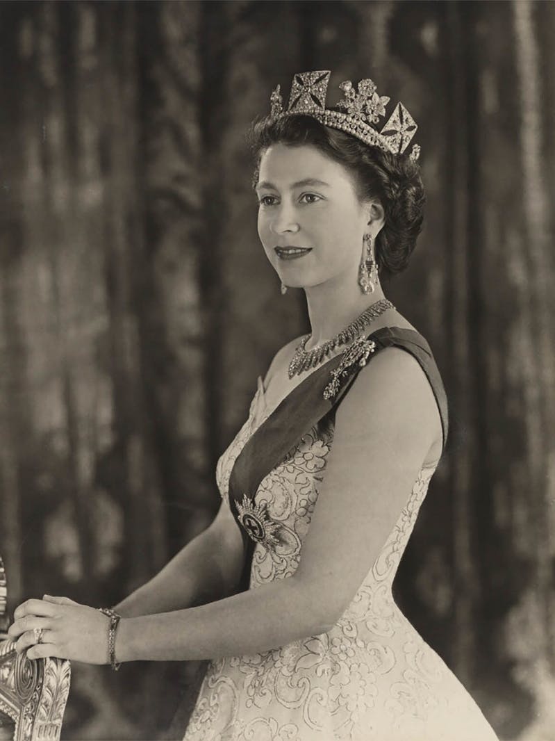 A black and white photo of queen Eliabeth ii standing in white dress diadem with watch bracelet clearly visibile on her left wrist