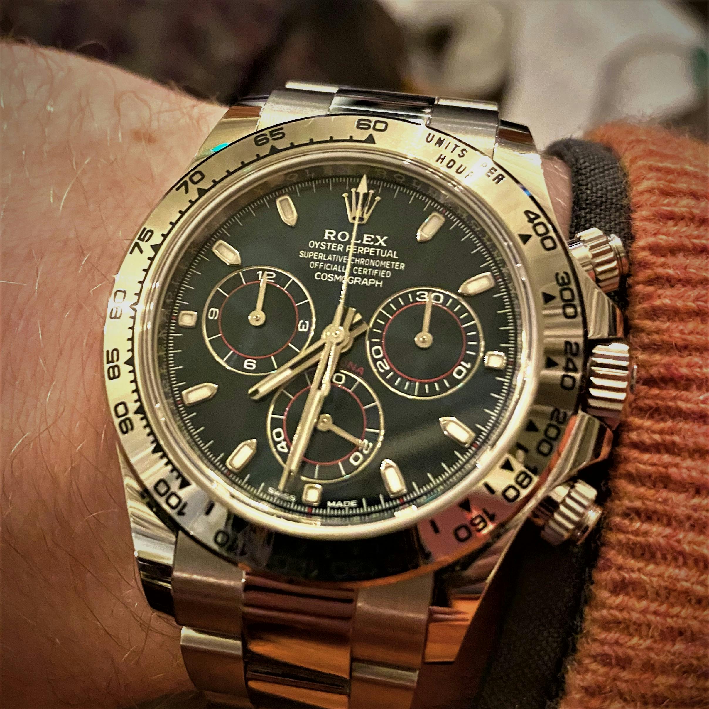 A white gold Rolex Daytona with a dark bluew dial and white gold hands and indices with red accents on the subdials, a white gold bezel with a tachymeter and a white gold braclet on someone's wrist.