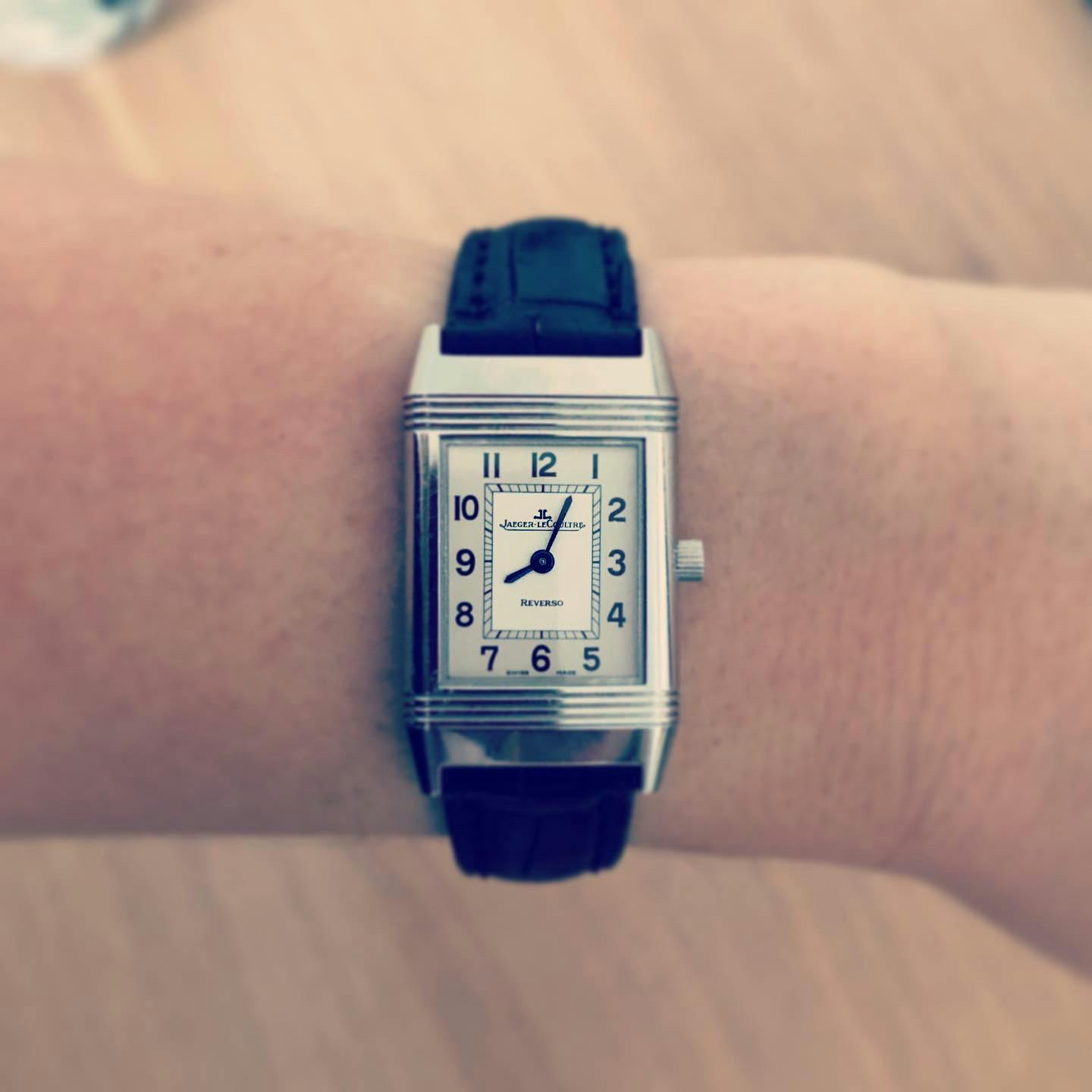Small rectangular wristwatch on a wrist with silver and white dial and black hands and numerals on a black strap