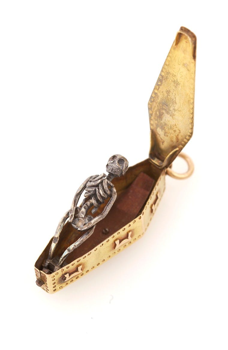 A gold memento mori pendant, used to remind the user of the transience of life and material luxury, containing a decaying corpse inside a coffin. (Open).