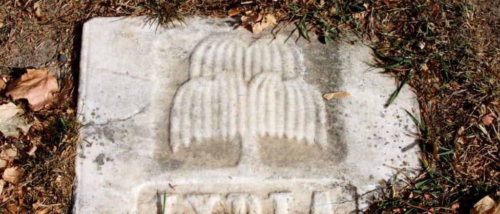 Detail of a white stone laid onto the ground, showing a simple carving of a weeping willow tree.