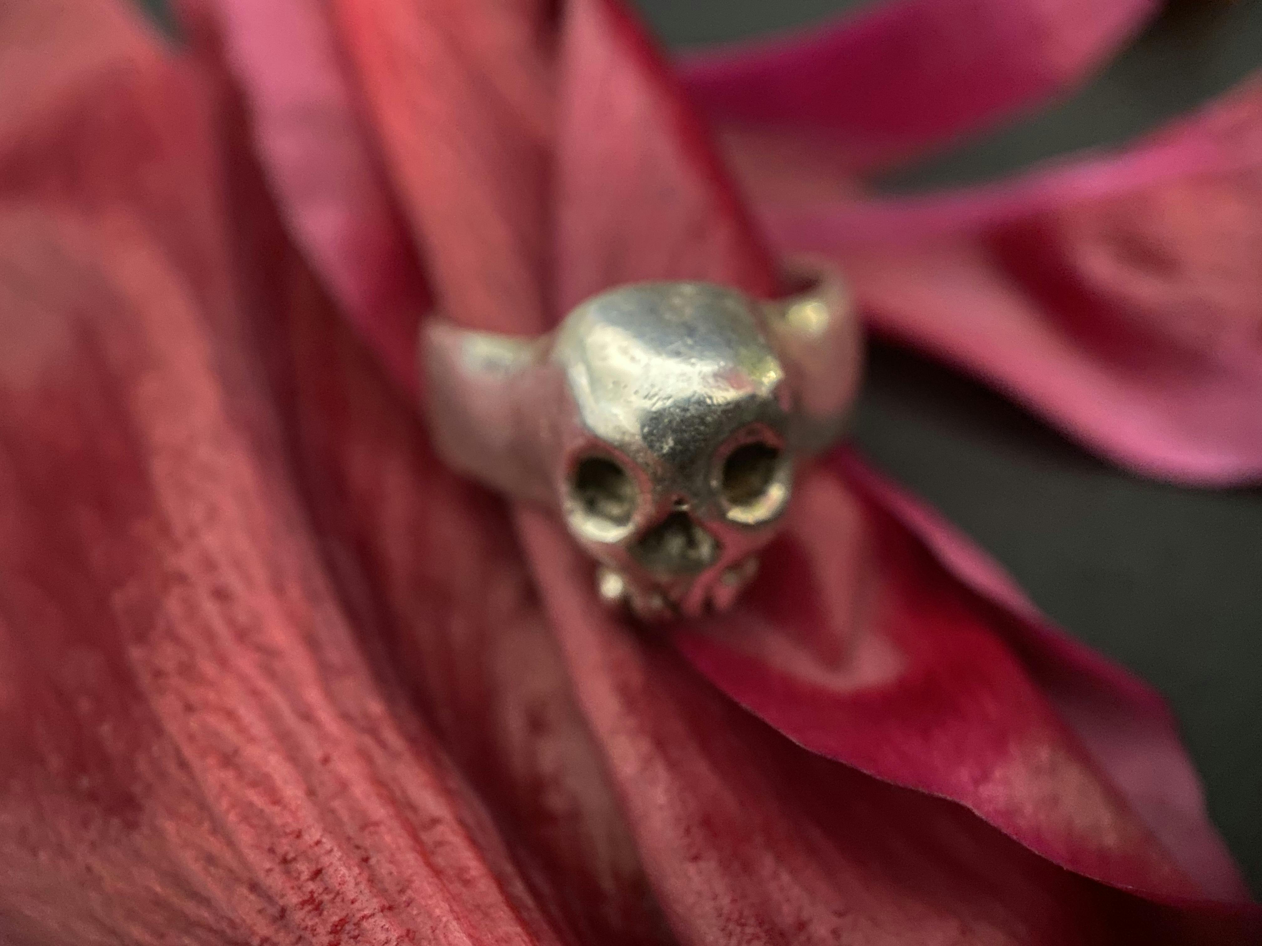 A small simple skull face on the front of a silver band, worn on a flower petal like a ring 