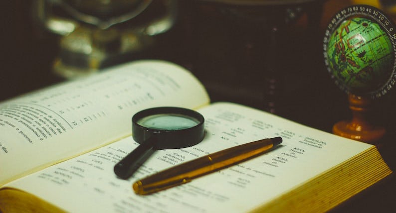 Image of a magnifying glass and pen atop the pages of an open book next to a small globe.