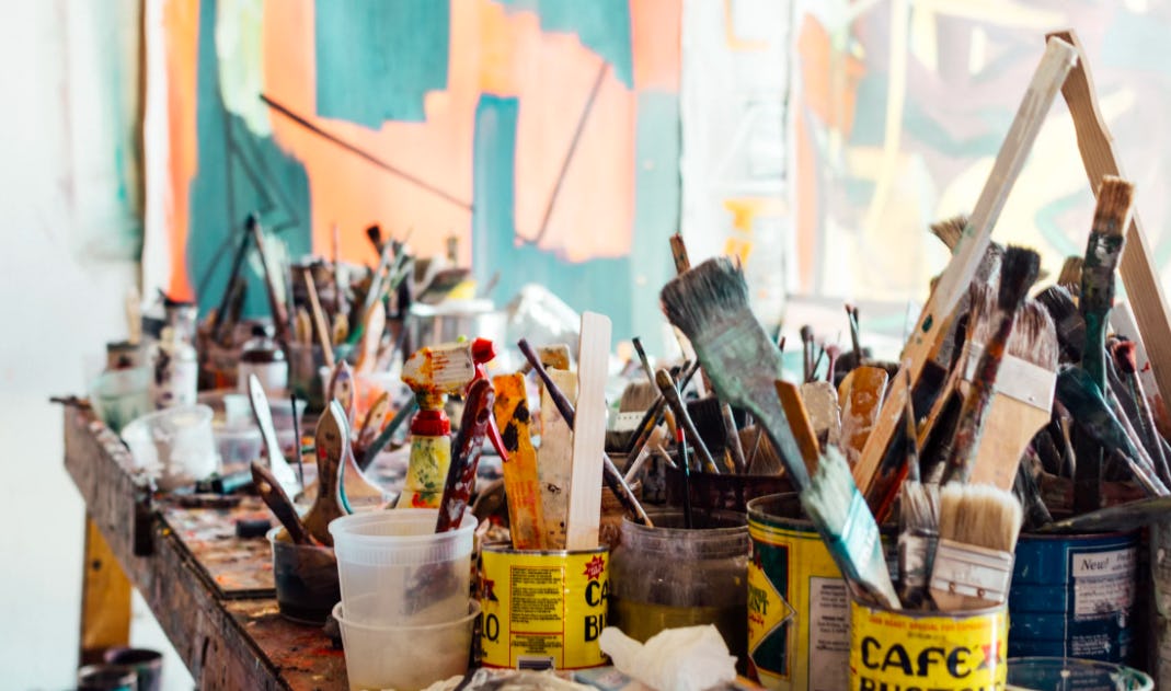 A photo of a painter’s workbench, littered with brushes, tools, and paint splotches