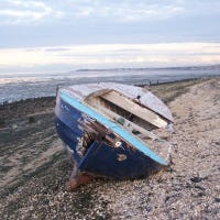 a photo of a battered boat, apparently washed ashore