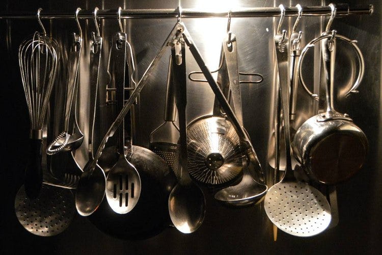 metal cooking utensils hanging against a stainless steel backdrop