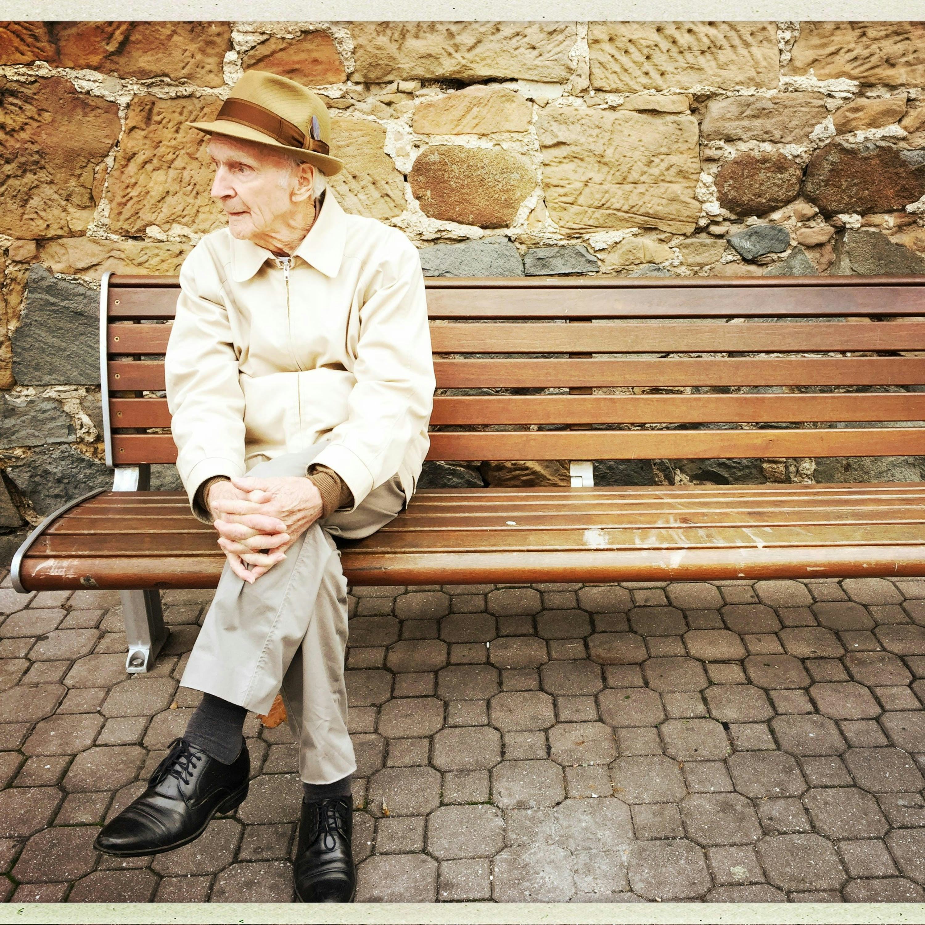 photo of an elderly man sitting on one end of a bench, legs crossed. Photo by Helene Thomas