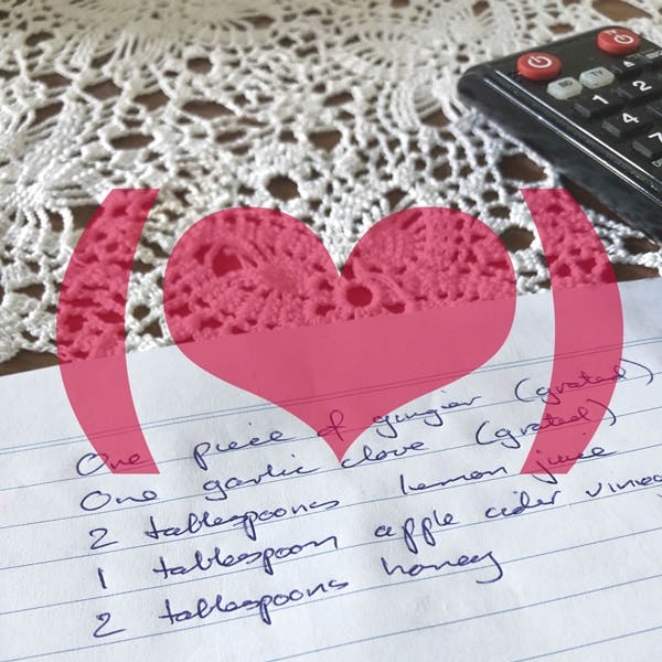 A pink translucent heart icon in parentheses, against a photo: a wooden surface covered in a lace doily, and on it, a TV remote control and a piece of notebook paper with the following written on it: ‘One piece of ginger (grated); one garlic clove (grated); 2 tablespoons lemon juice; 1 tablespoon apple cider vingar; 2 tablespoons honey’