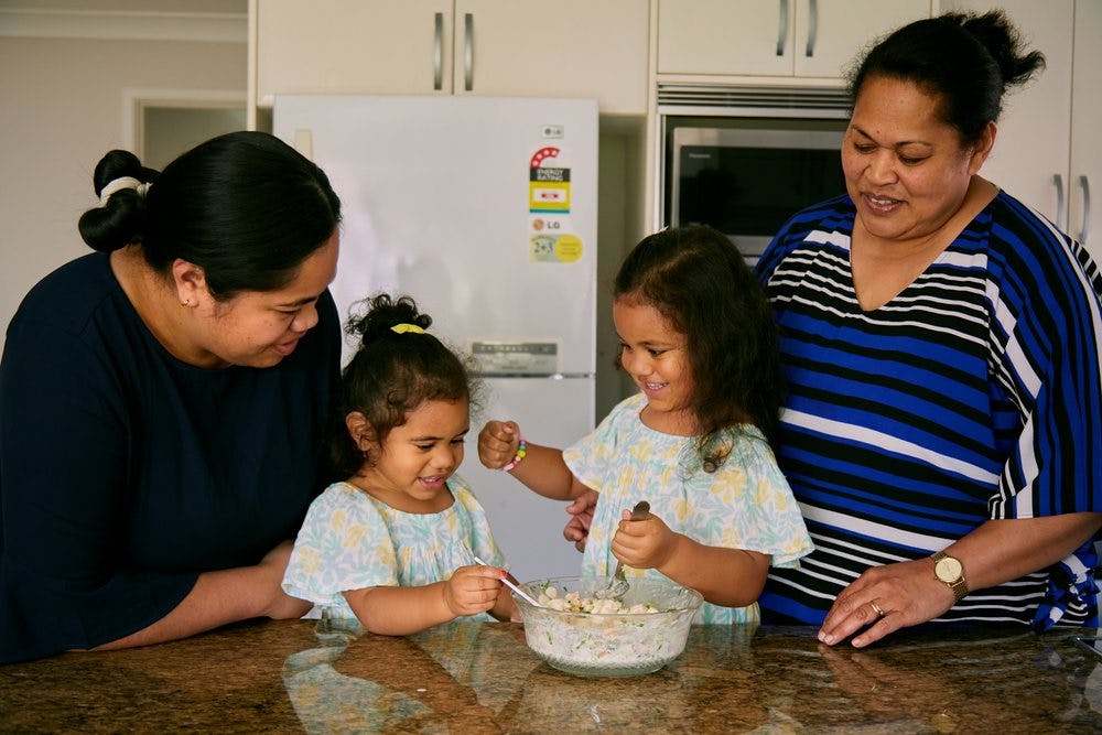 Sela Atiola stands to the left of her kitchen bench with her daughters in the centre and her mother to the far right. They make 'ota ika together with smiles on their faces. Photograph: Sherry Zheng.