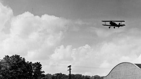 Men watch a biplane fly over the hangar at the Kenyon College School of Aeronautics.