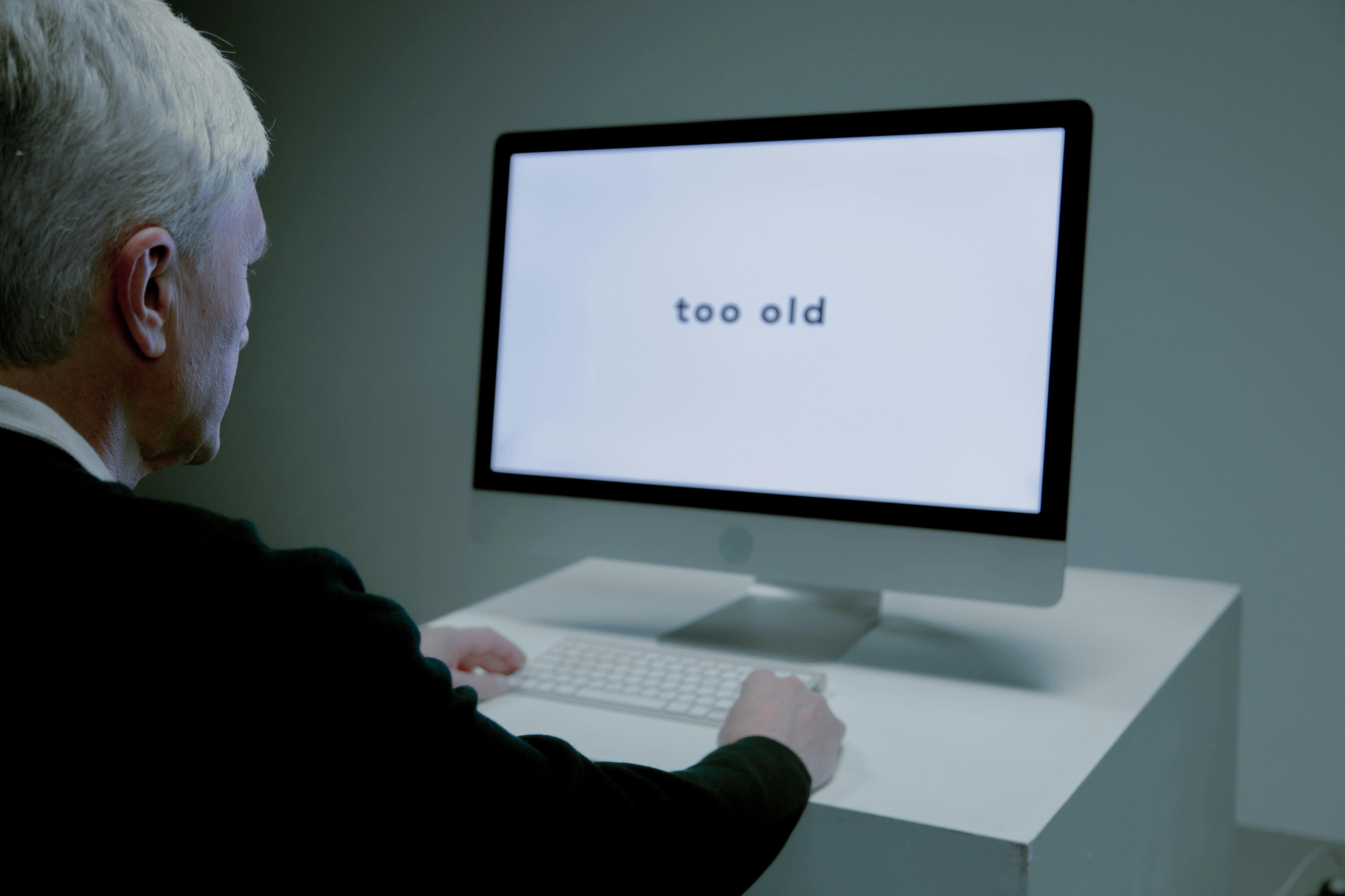 Old man reading "too old" text on his computer screen