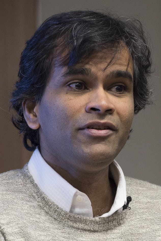 Sendhil Mullainathan: A person with dark hair and a light complexion speaks, wearing a white shirt and grey sweater, indoors against a neutral background.