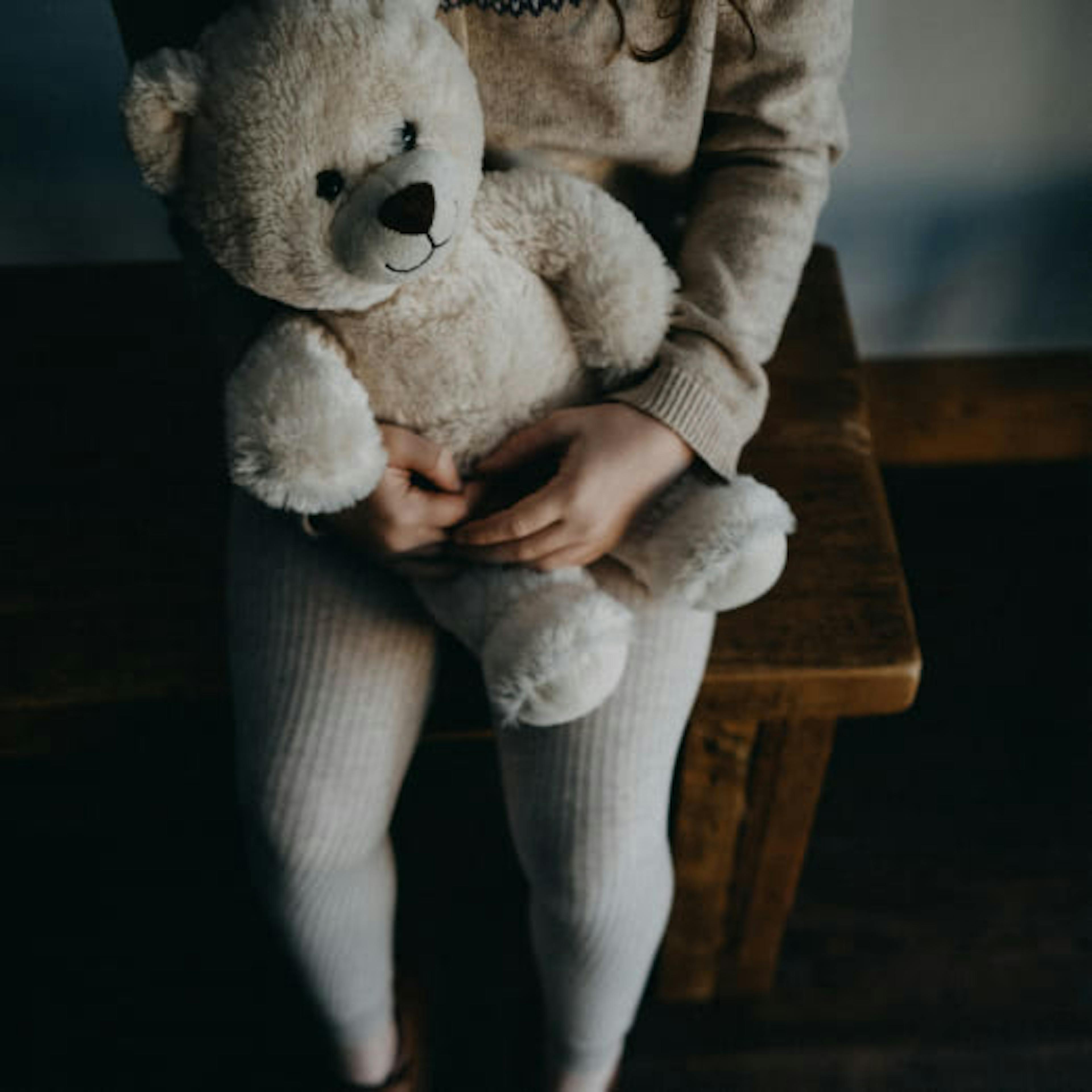 A little girl waits with her teddy bear for her mother to pay attention to her.