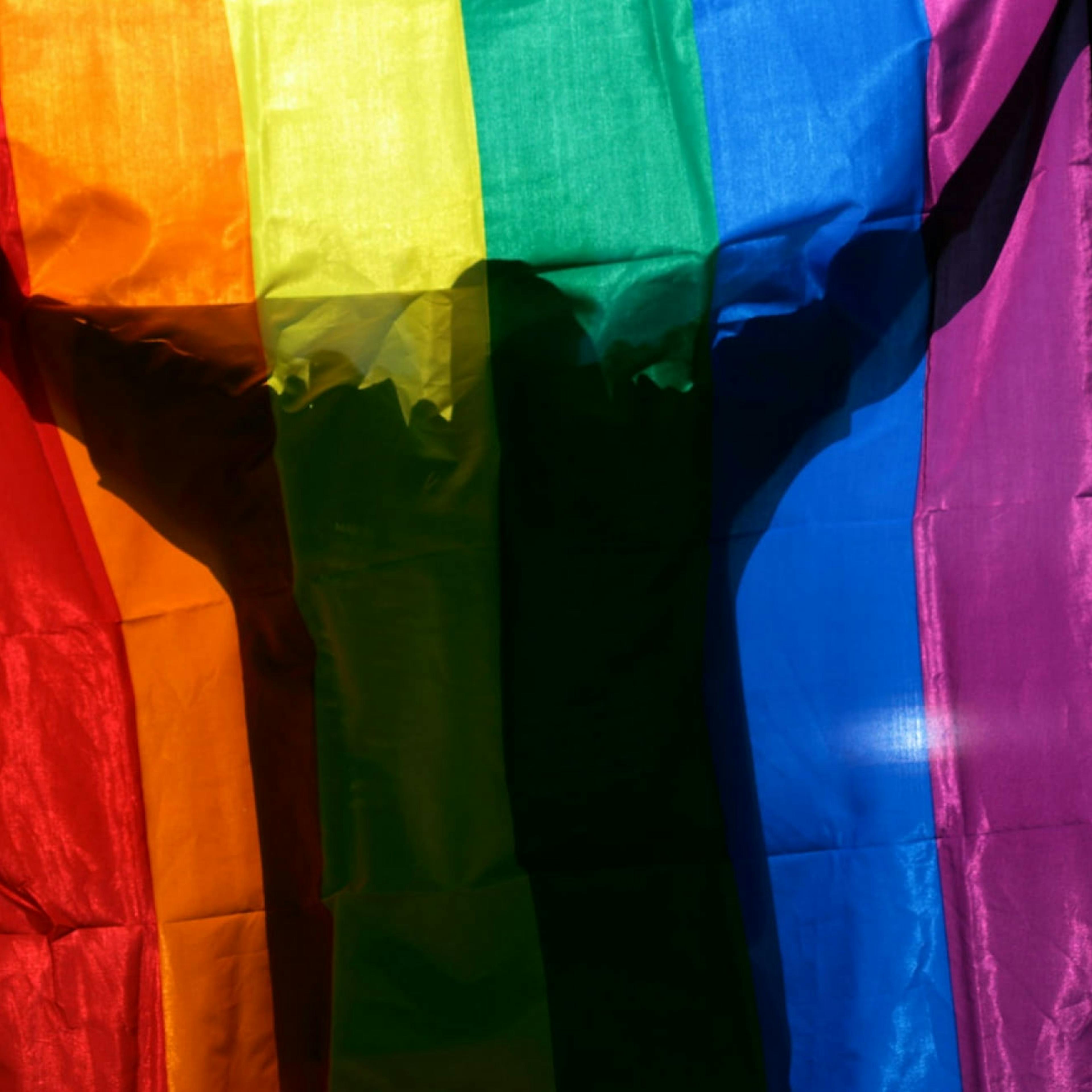 An LGBTQ+ person hides behind a rainbow flag.