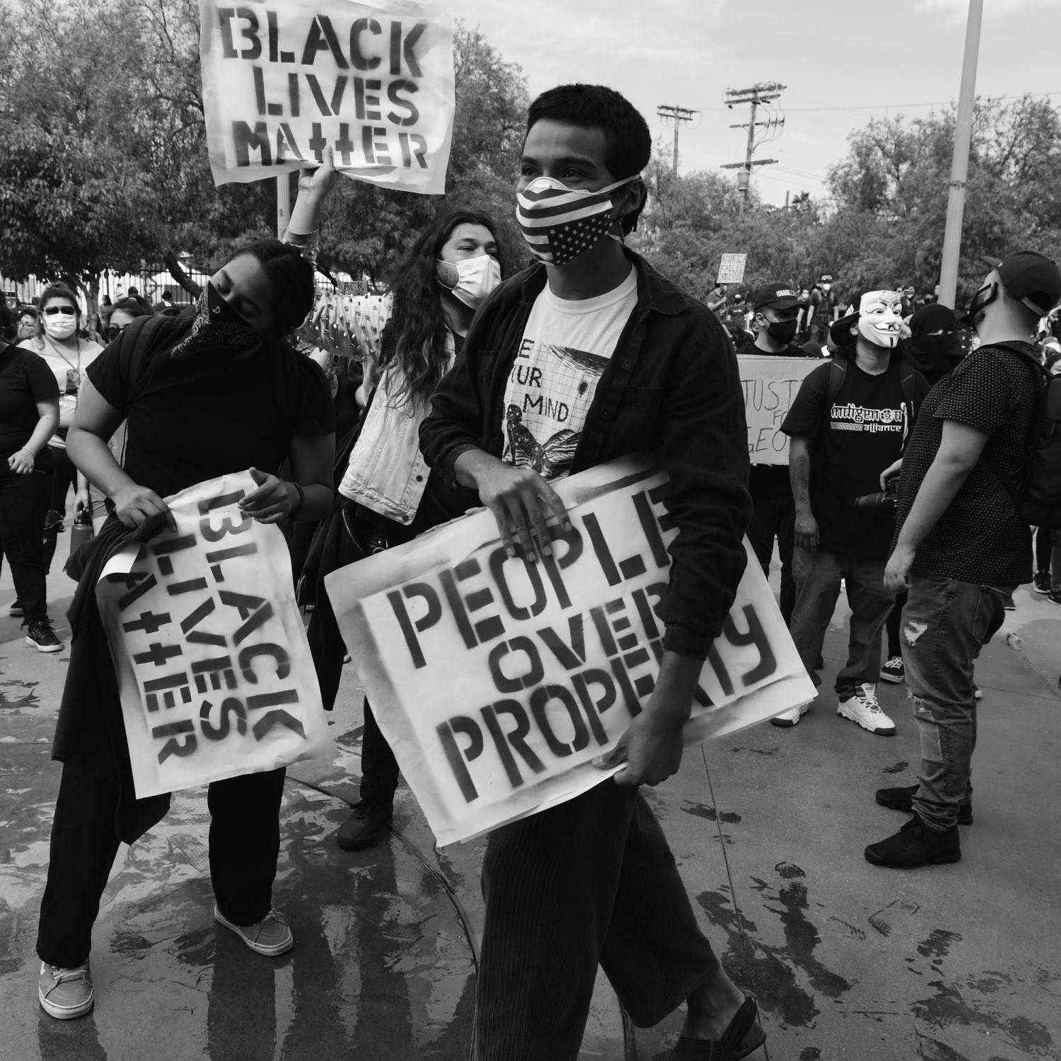 A protestor walks through a crowd with a sign that reads "People Over Property"