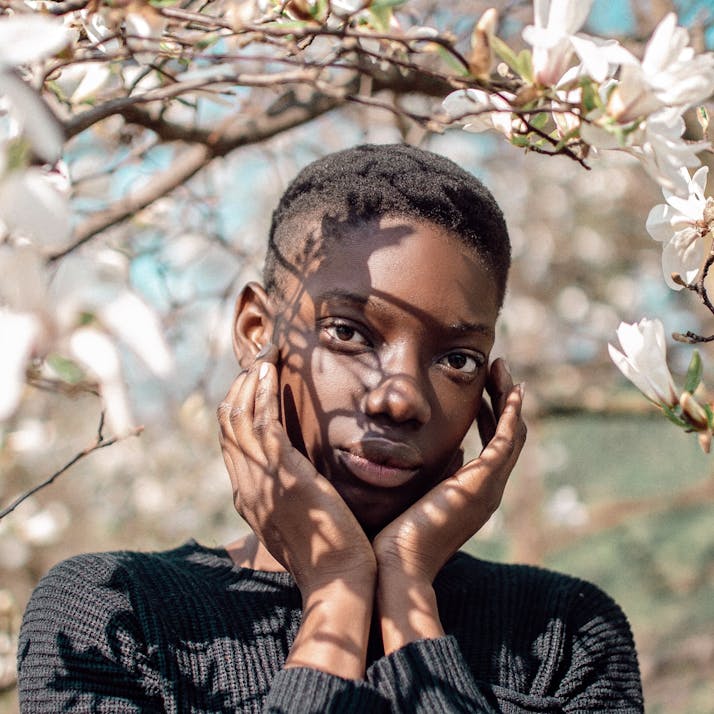 A young adult standing with his hands on his face, under a flowering tree.