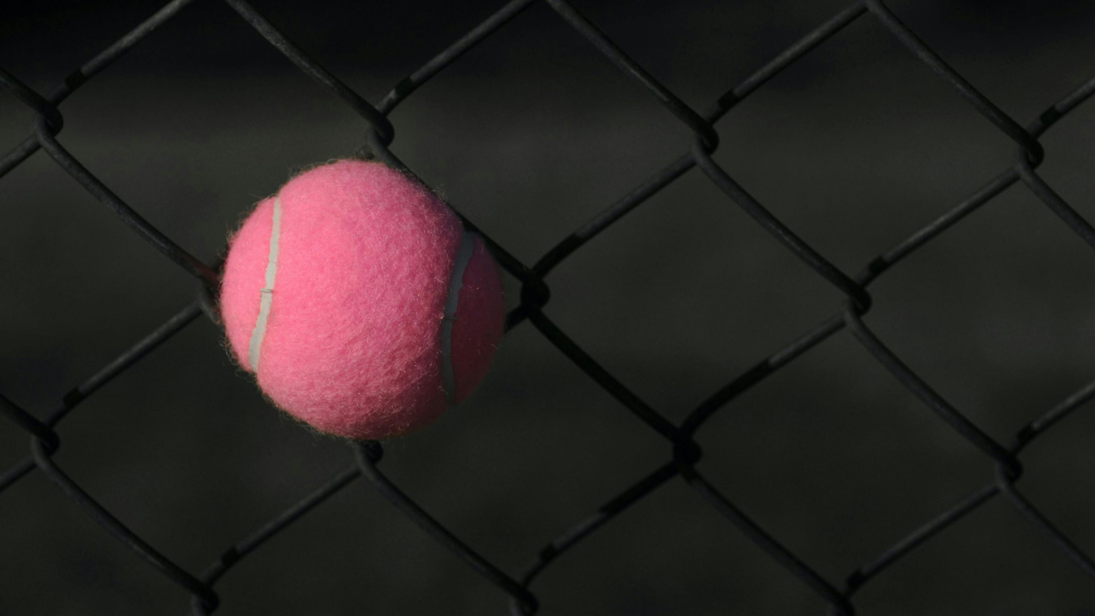 A tennis ball stuck in the hole of a chain link fence.